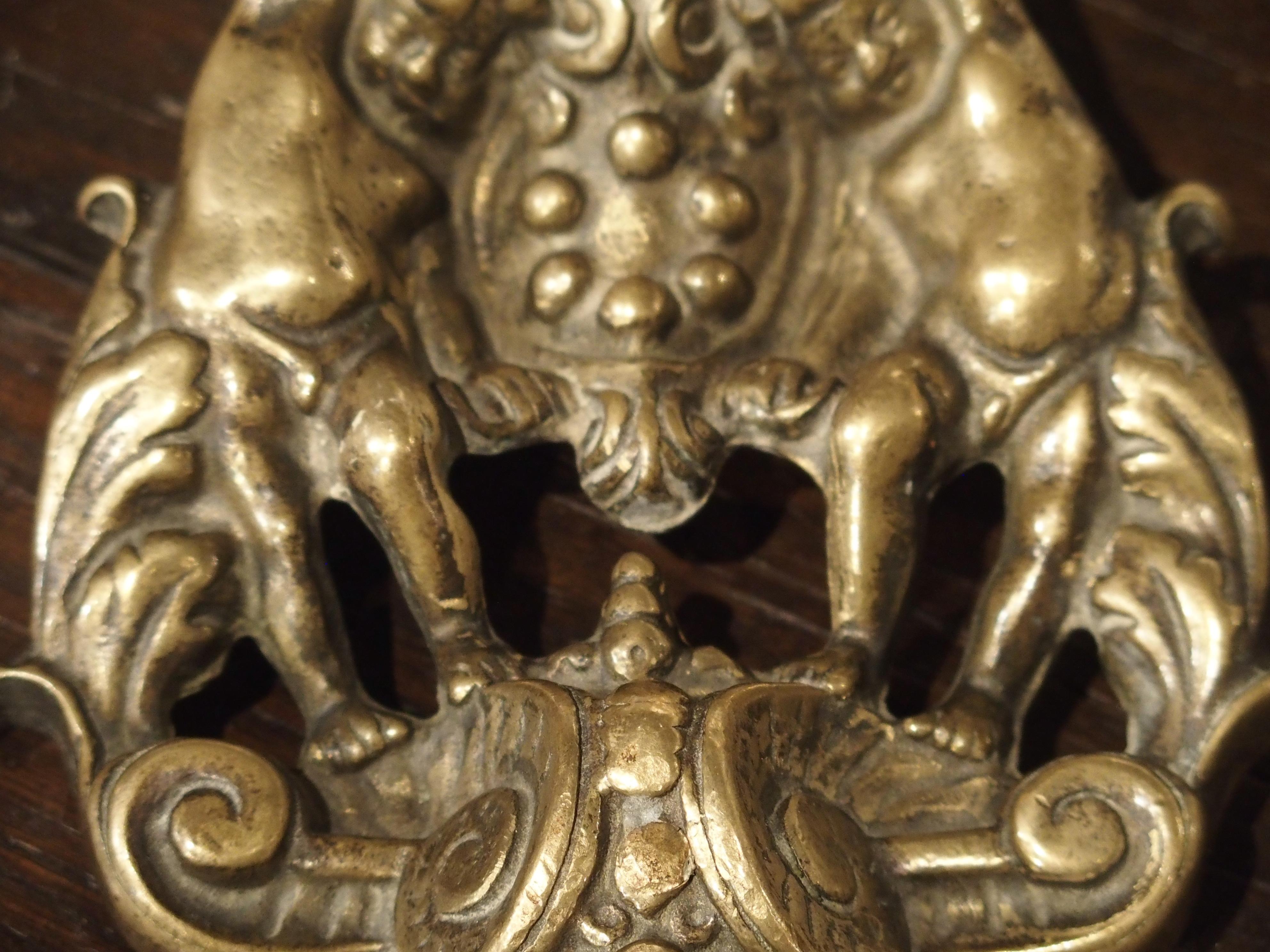 Produced in Italy in the late 1800s, this impressive bronze dore door knocker contains various Classic design elements including putti, a coat of arms, and a large mascaron. Similar door knockers were first produced in Italy during the