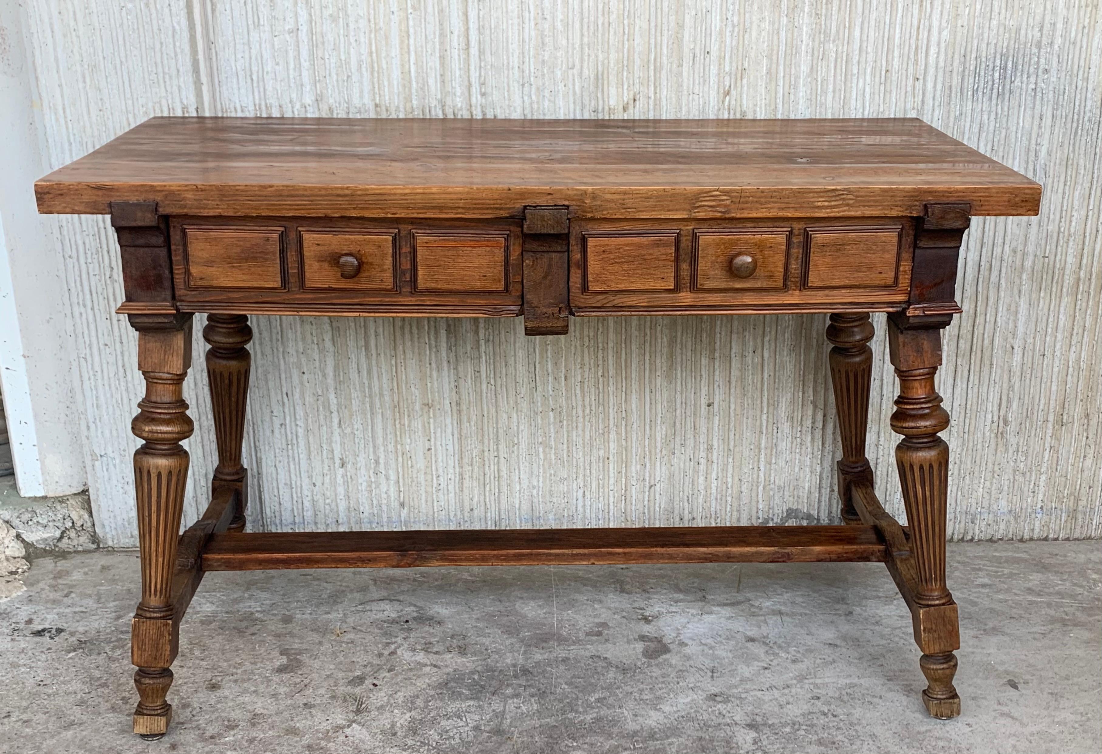 An 19th century Spanish baroque desk, or writing table made of solid oak with fluted shaped legs joined by solid wood stretched. Two drawers with original iron drawer pulls and two false drawers in back. The top is made from a single plank of oak