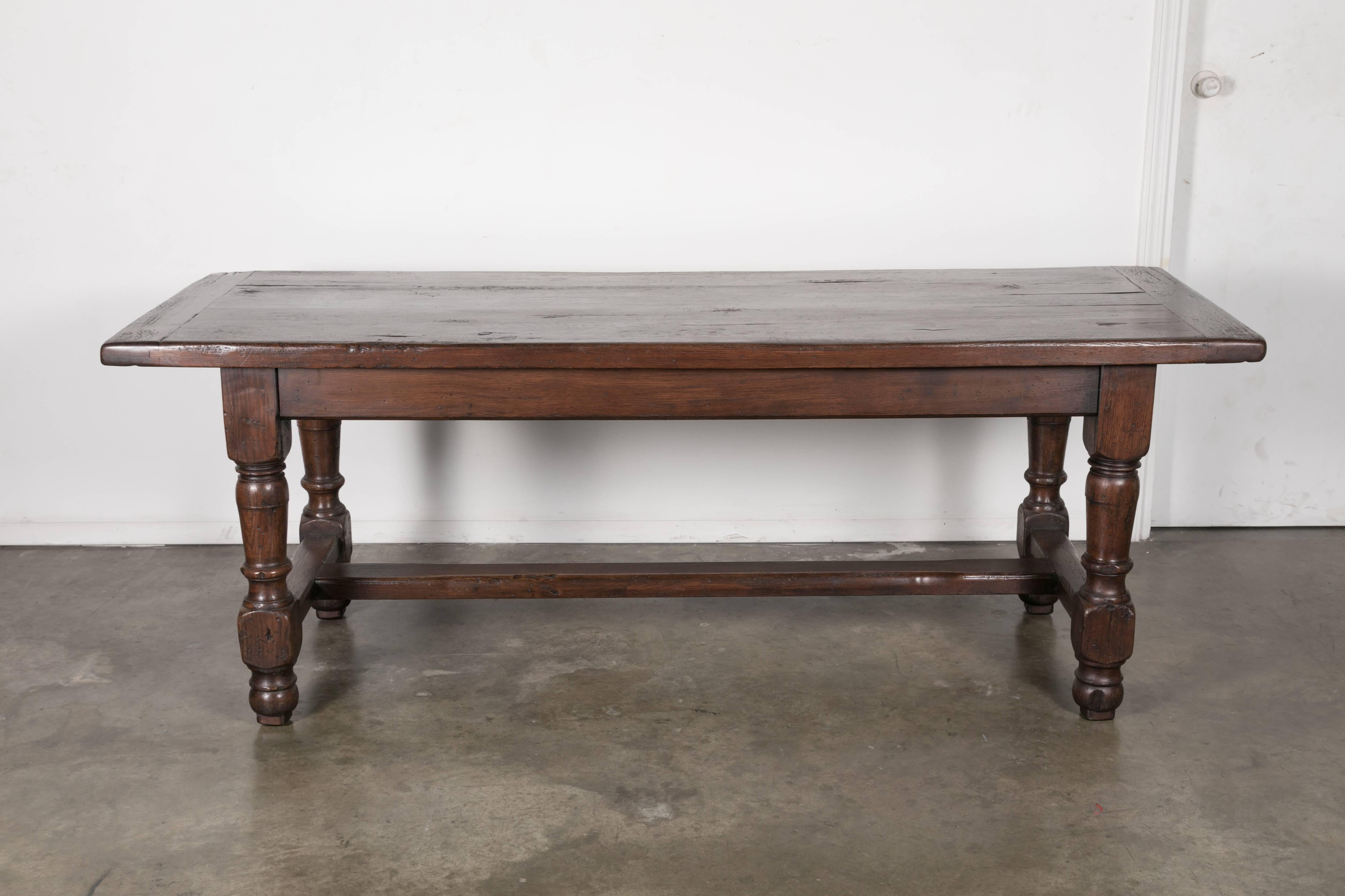 19th century French Louis Philippe farm table, circa 1890s, in solid oak from the Normandie region. It has a rectangular plank top with a drawer on one end, resting on four turned legs joined by an H-stretcher. Handsome grain pattern with rich,