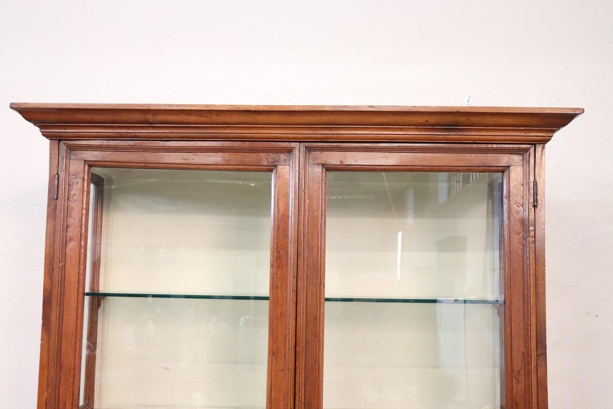 Vitrine italienne ancienne en bois de noyer massif et verre. Très linéaire et essentiel, il est parfait pour être combiné même dans une maison moderne. La partie inférieure est équipée d'une porte en verre avec une ouverture à rabat particulière.