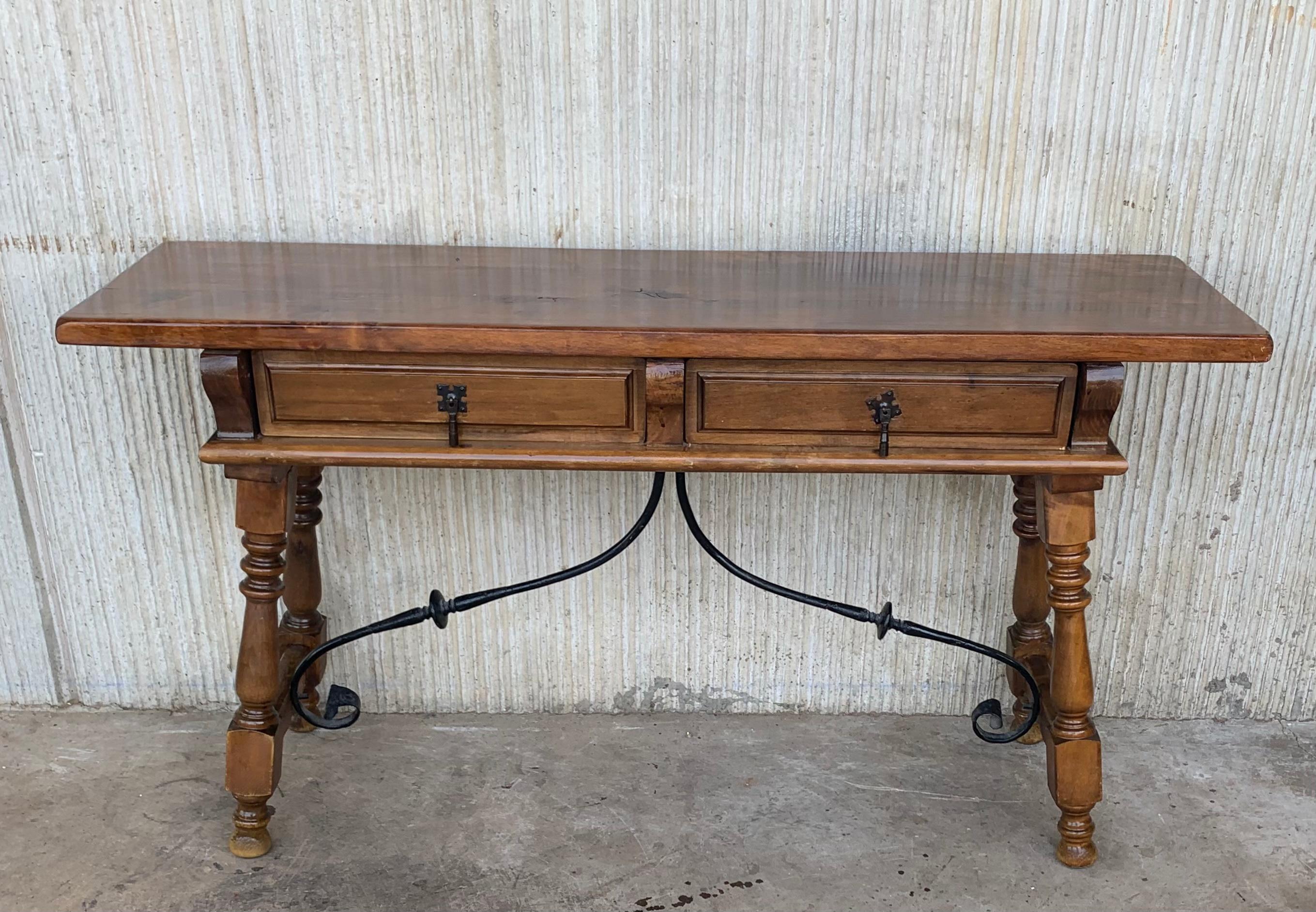 An 19th century Spanish baroque desk, or writing table made of solid walnut with lyre shaped legs joined by wrought iron stretchers. Hand carved decoration across the front and the back. Two drawers with original iron drawer pulls. The top is made