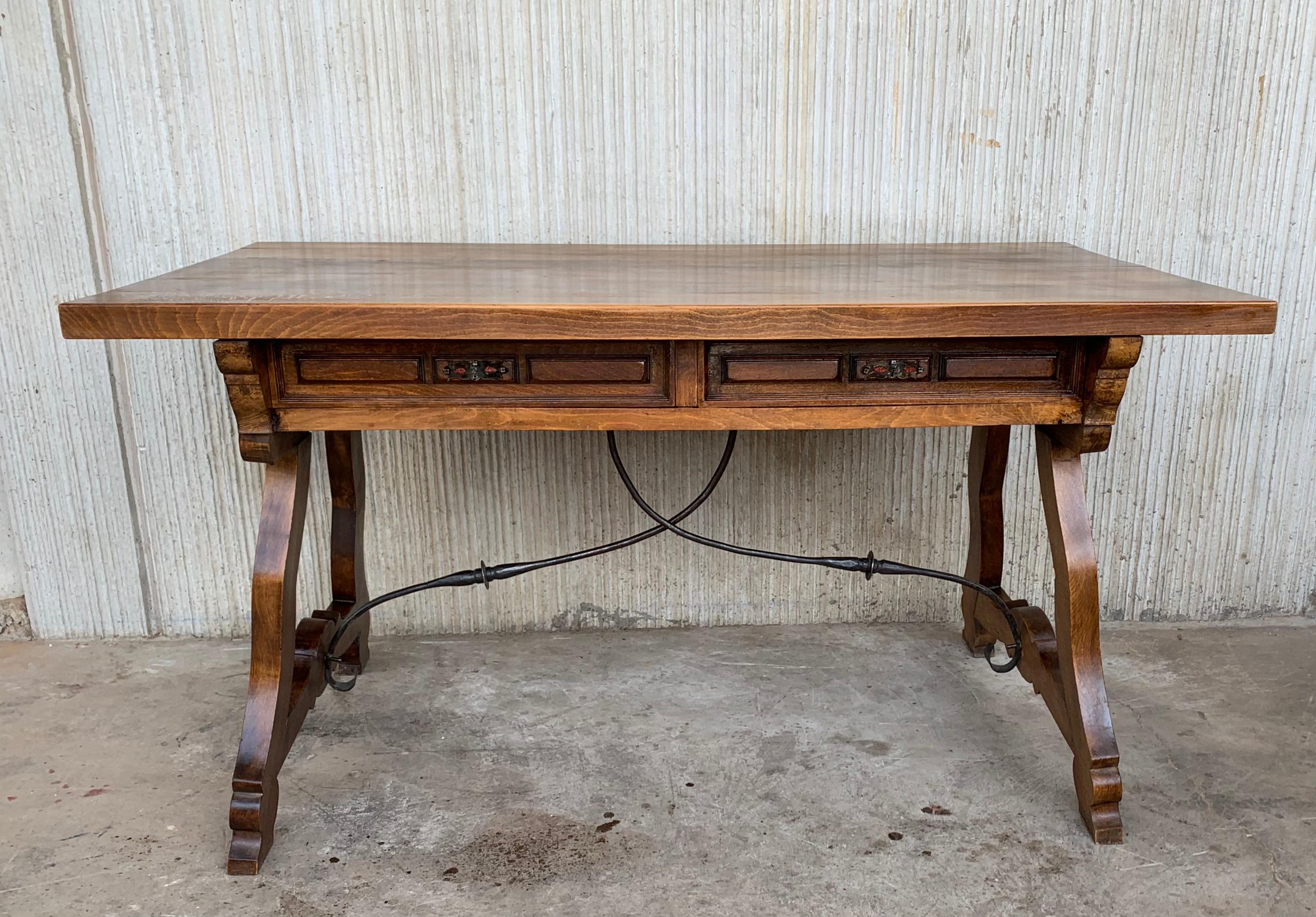 An 19th century Spanish baroque desk, or writing table made of solid walnut with lyre shaped legs joined by wrought iron stretchers. Two drawers with original iron drawer pulls. The top is made from a single plank of walnut and is slightly warped.