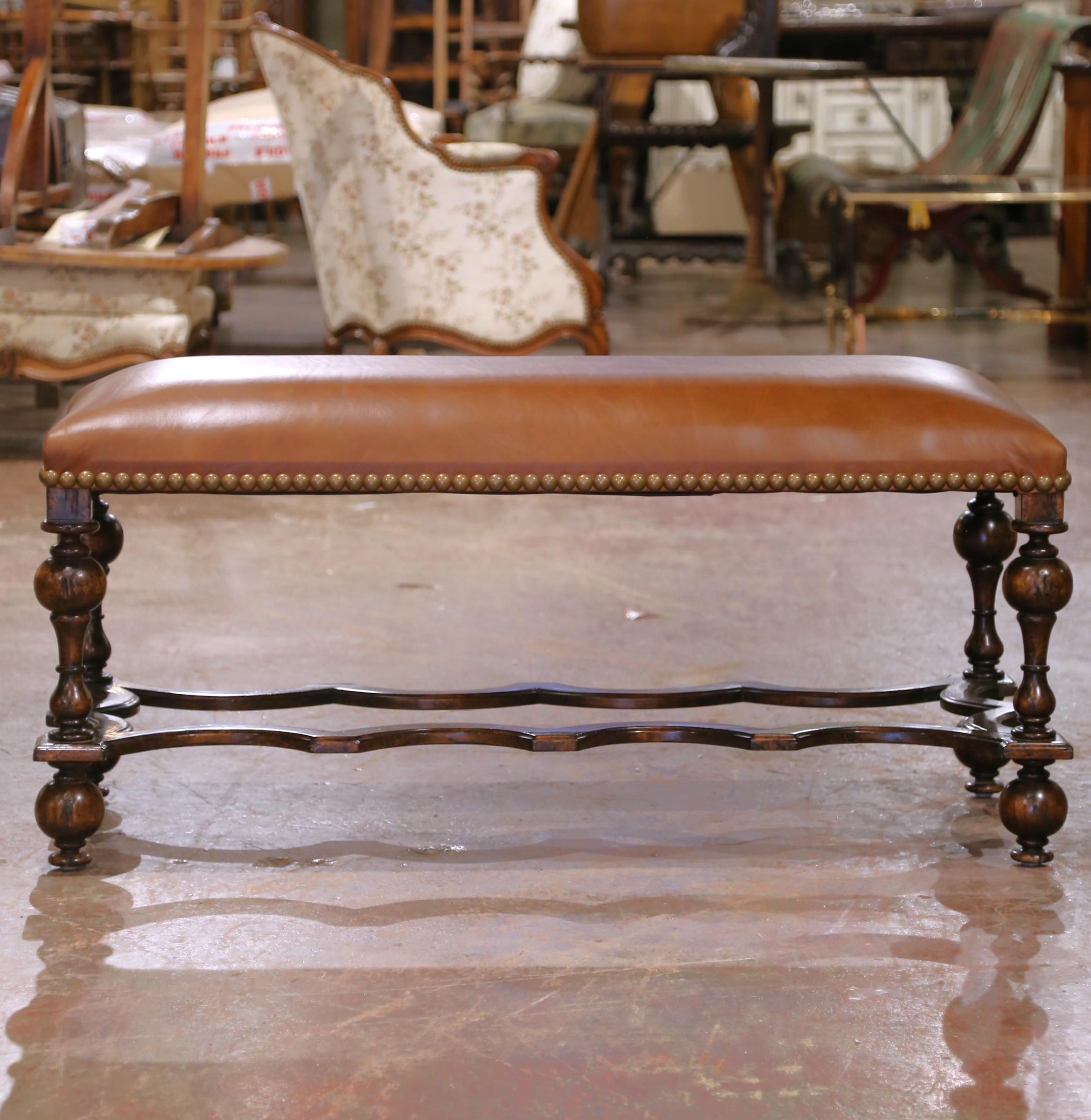 This bold and elegant antique bench was crafted in Spain circa 1880 and exhibits strong Baroque design influences. Built from richly grained walnut, the piece features turned baluster legs connected by an eye-catching serpentine stretcher, an iconic