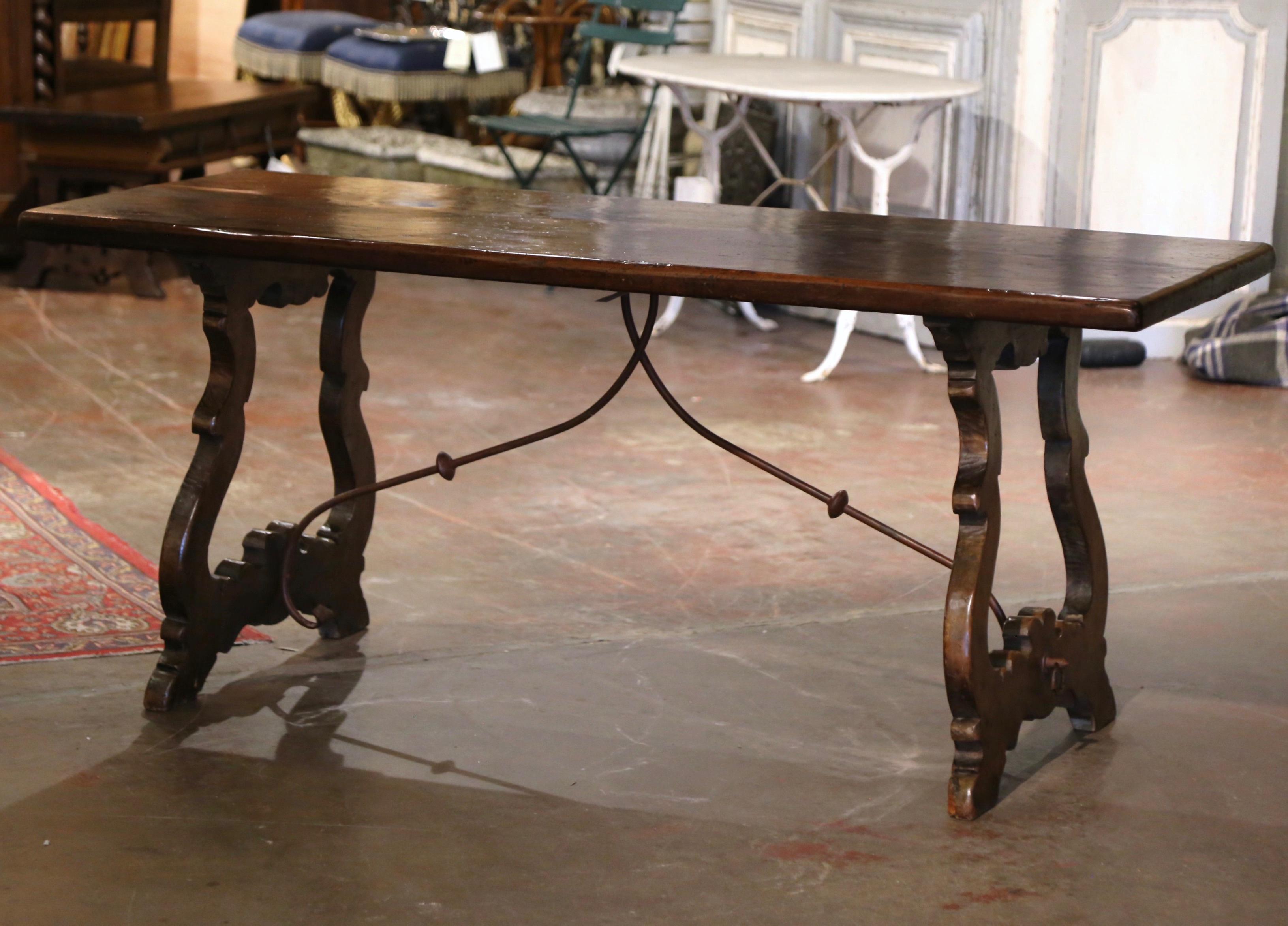 Decorate a dining or breakfast room with this elegant six foot antique table. Carved in Spain circa 1880, the trestle table stands on two intricate carved ox yoke leg supports, connected with a thick scrolled forged double iron stretcher. The