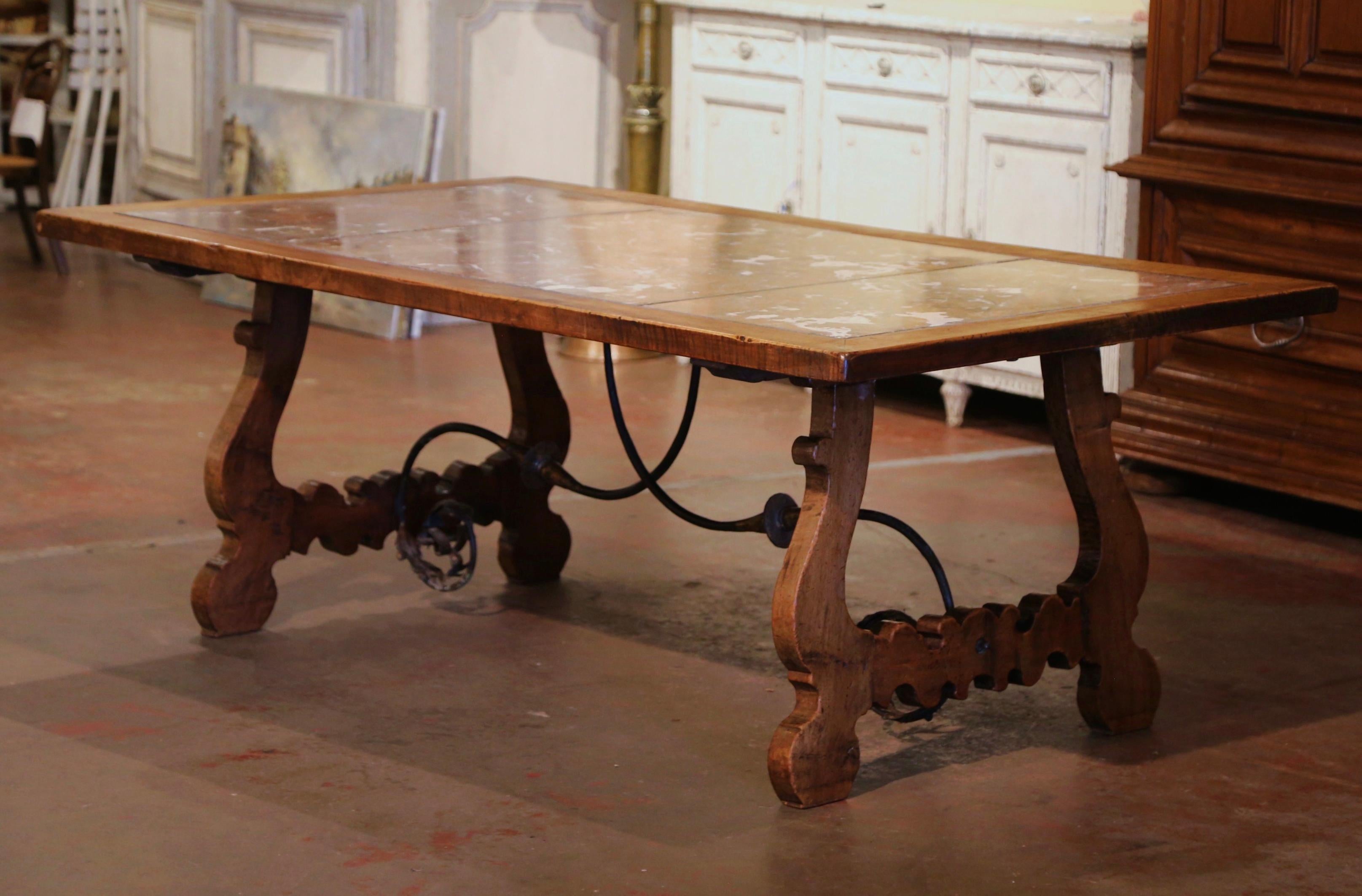 Decorate a dining or breakfast room with this elegant antique table. Carved in Spain circa 1870, the large trestle table stands on two intricate carved legs, connected with a thick scrolled forged foliate iron stretcher. The top is dressed with