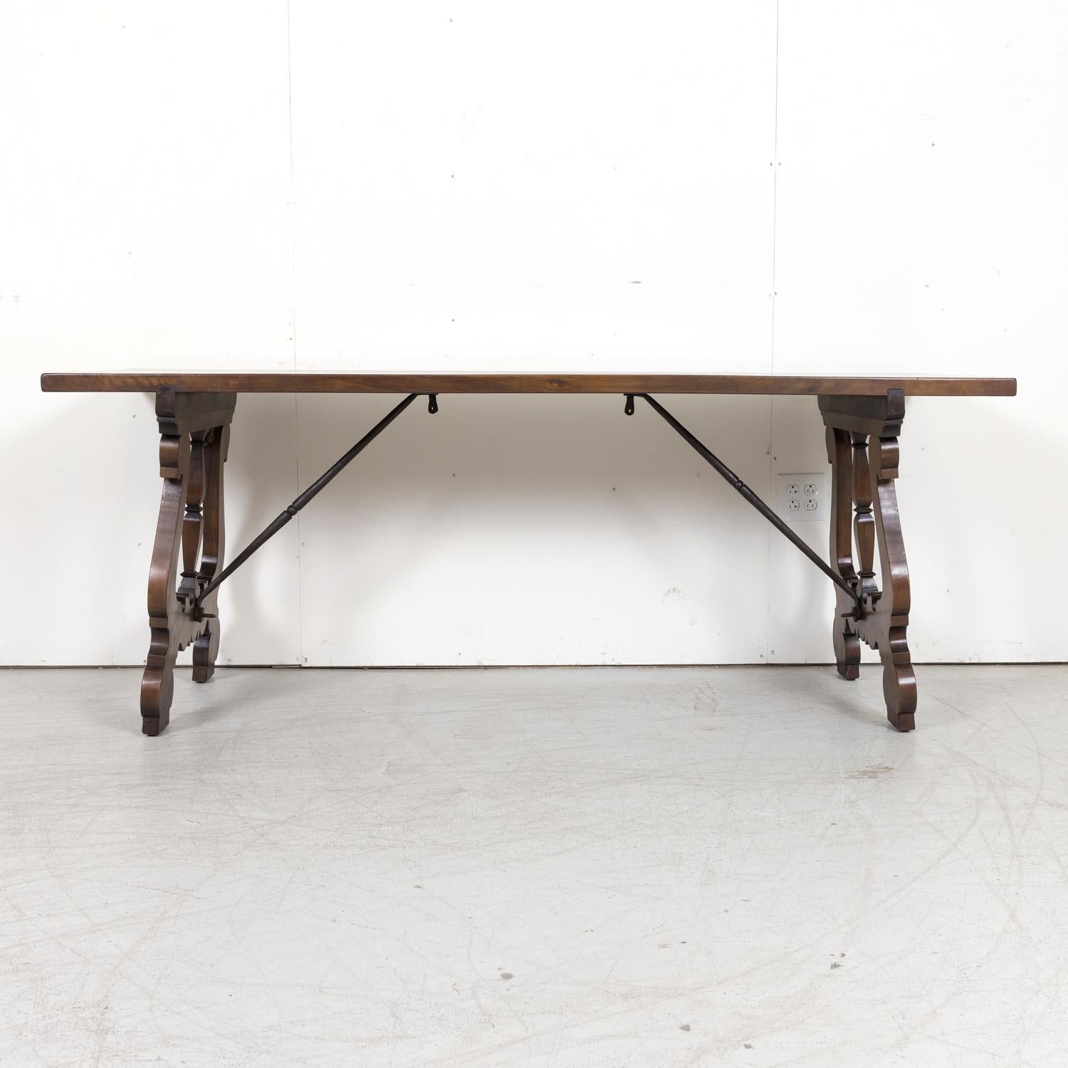A 19th century Spanish Baroque style trestle dining table handcrafted of walnut near Barcelona, circa 1890s. Having a rectangular two-plank top resting on beautifully carved lyre legs joined together by hand forged iron stretchers, this handsome