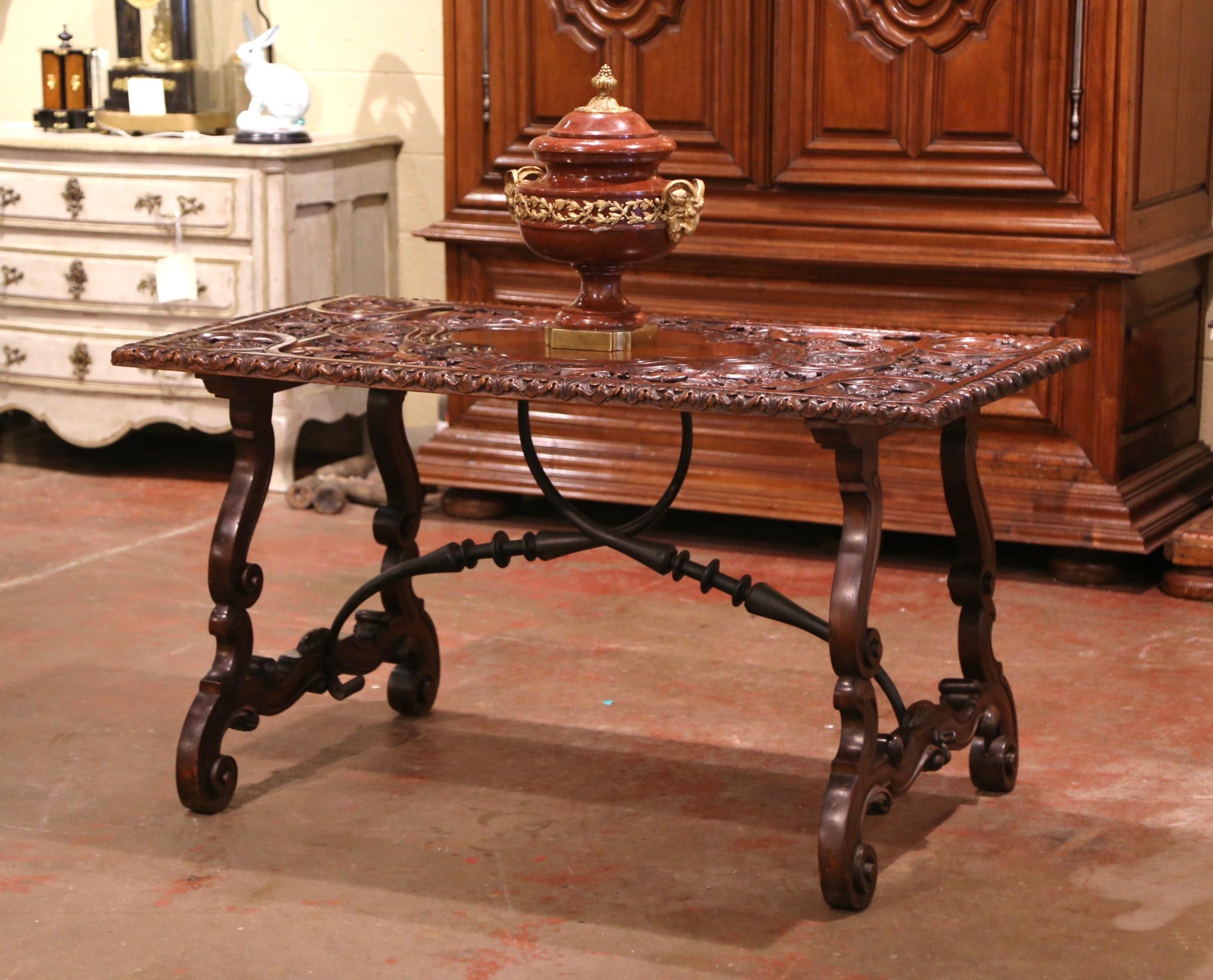 Decorate an entry with this elegant and richly sculpted table. Crafted in Spain circa 1840, the antique table stands on two carved legs connected with two thick forged iron stretchers. The table top features high relief hand carved motifs all over