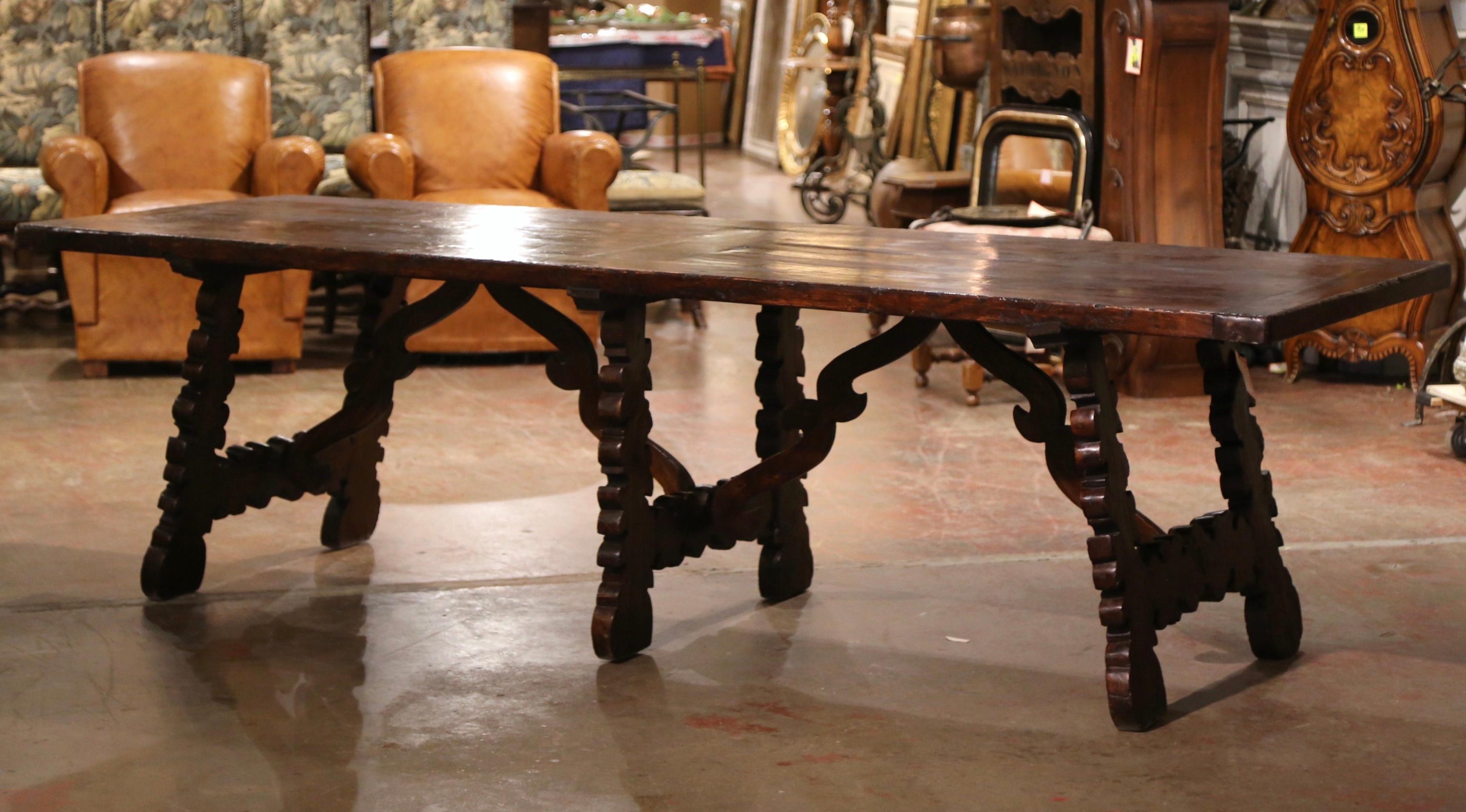 This elegant, antique dining room table was crafted in Spain, circa 1880. Almost 9 feet long, the table stands on three intricate scrolled pedestal legs, each connected with a carved cathedral form stretcher; the rectangular surface is dressed with