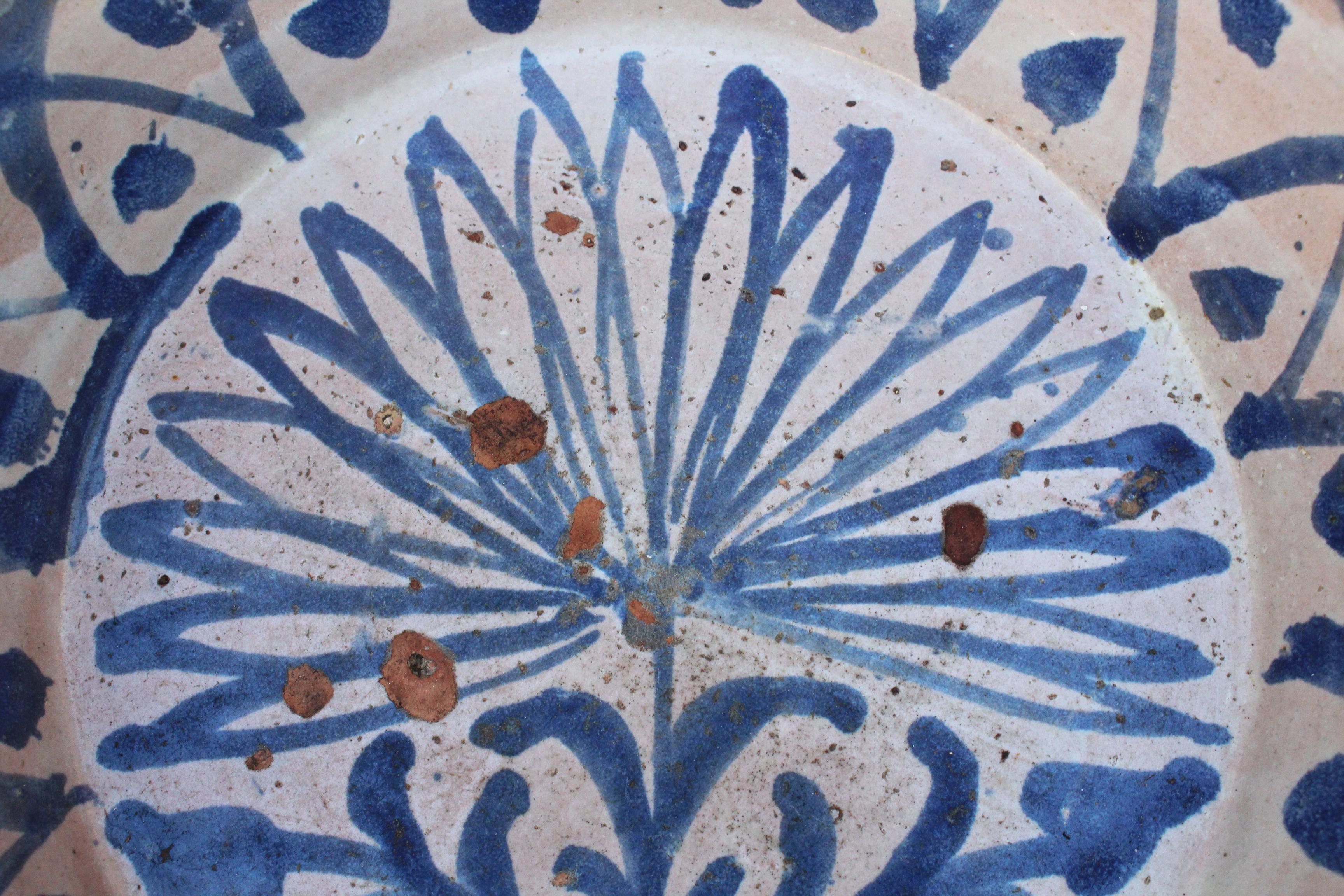 19th century Spanish Fajalauza white and blue glazed terracotta decorative plate painted with flowers. 

Fajalauza is a style that originates in Granada's Albaicín suburb, known for its mix of Christian and Al-Andalus cultures, as can be admired