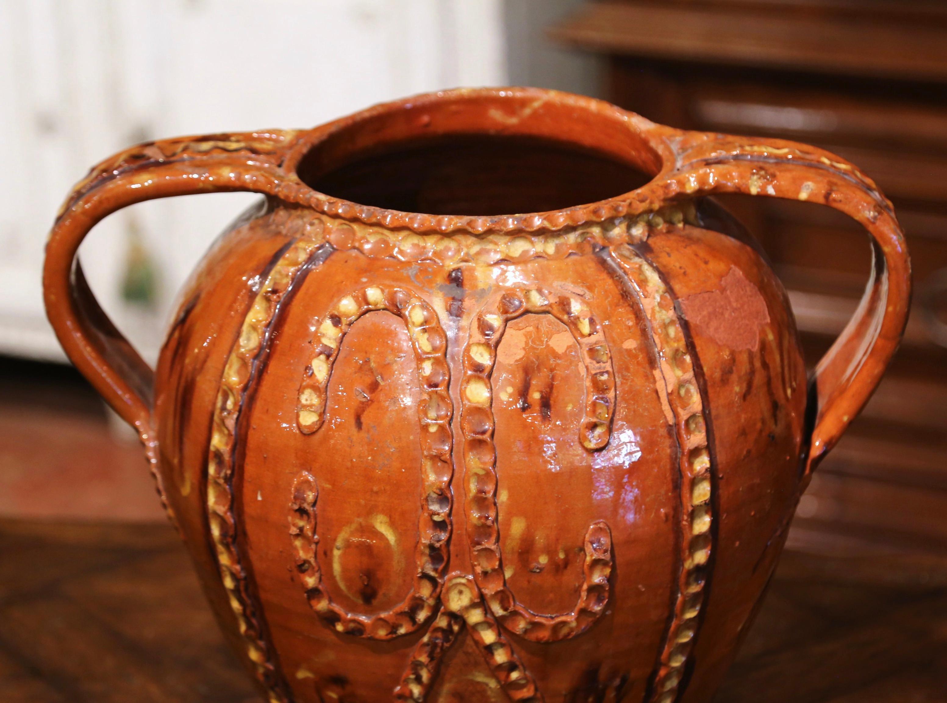 Decorate kitchen cabinets with this antique pottery olive oil pot. Created in Spain circa 1880 and made of terracotta with a brown glaze and beige hand painted motifs in high relief, the jug is round in shape and dressed with elegant side handles.