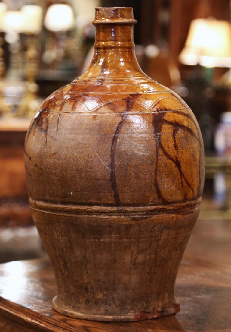 This antique pottery wine bottle was created in Spain circa 1880; made of terracotta with a dark beige glaze and hand painted motifs, the jug is round in shape with tall neck. The large wine holder is in excellent condition commensurate with age and