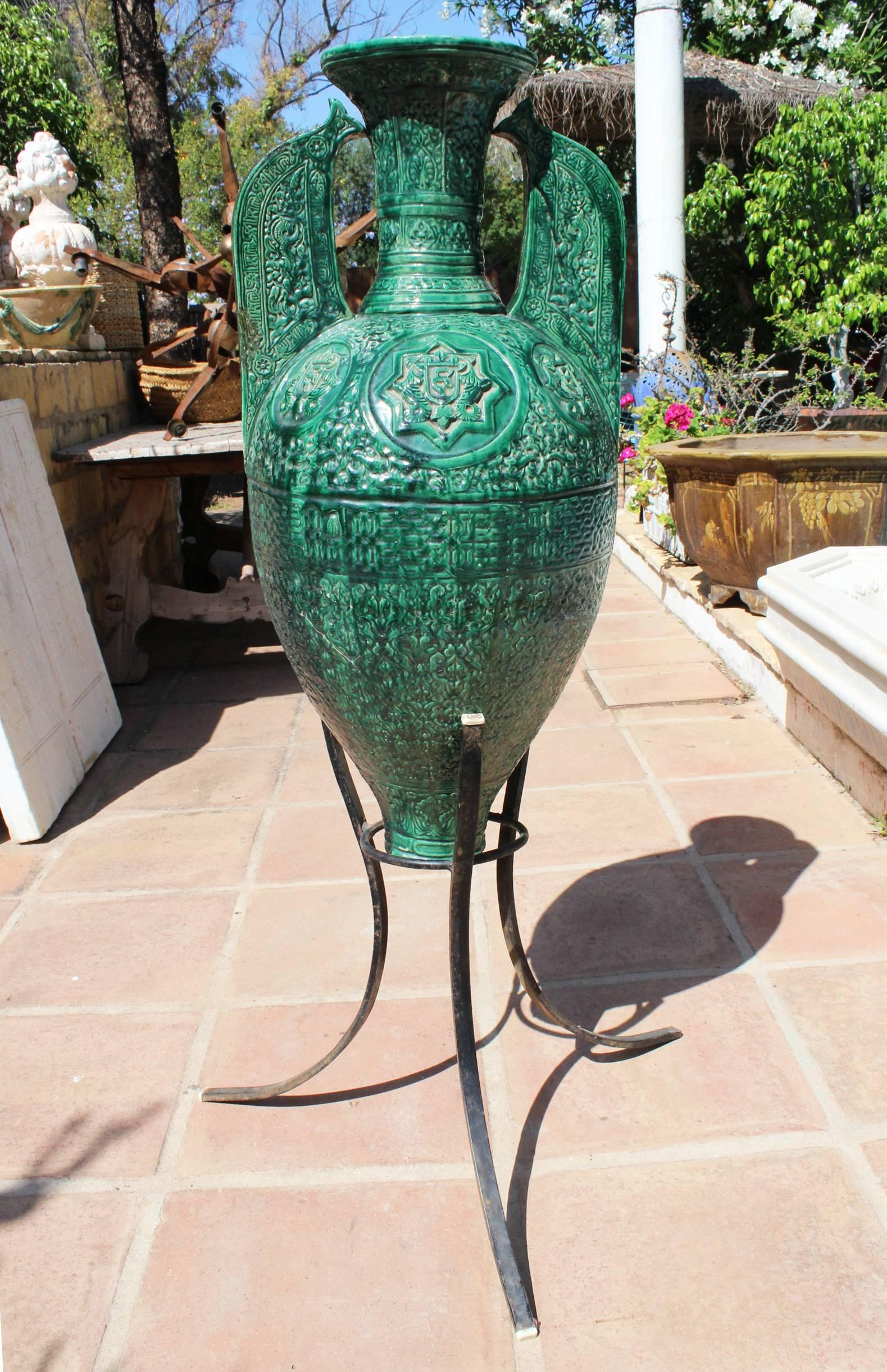 19th century Spanish green glazed ceramic Moorish style amphora on a three legged wrought iron pedestal. 

Iron pedestal height is 79 cm.