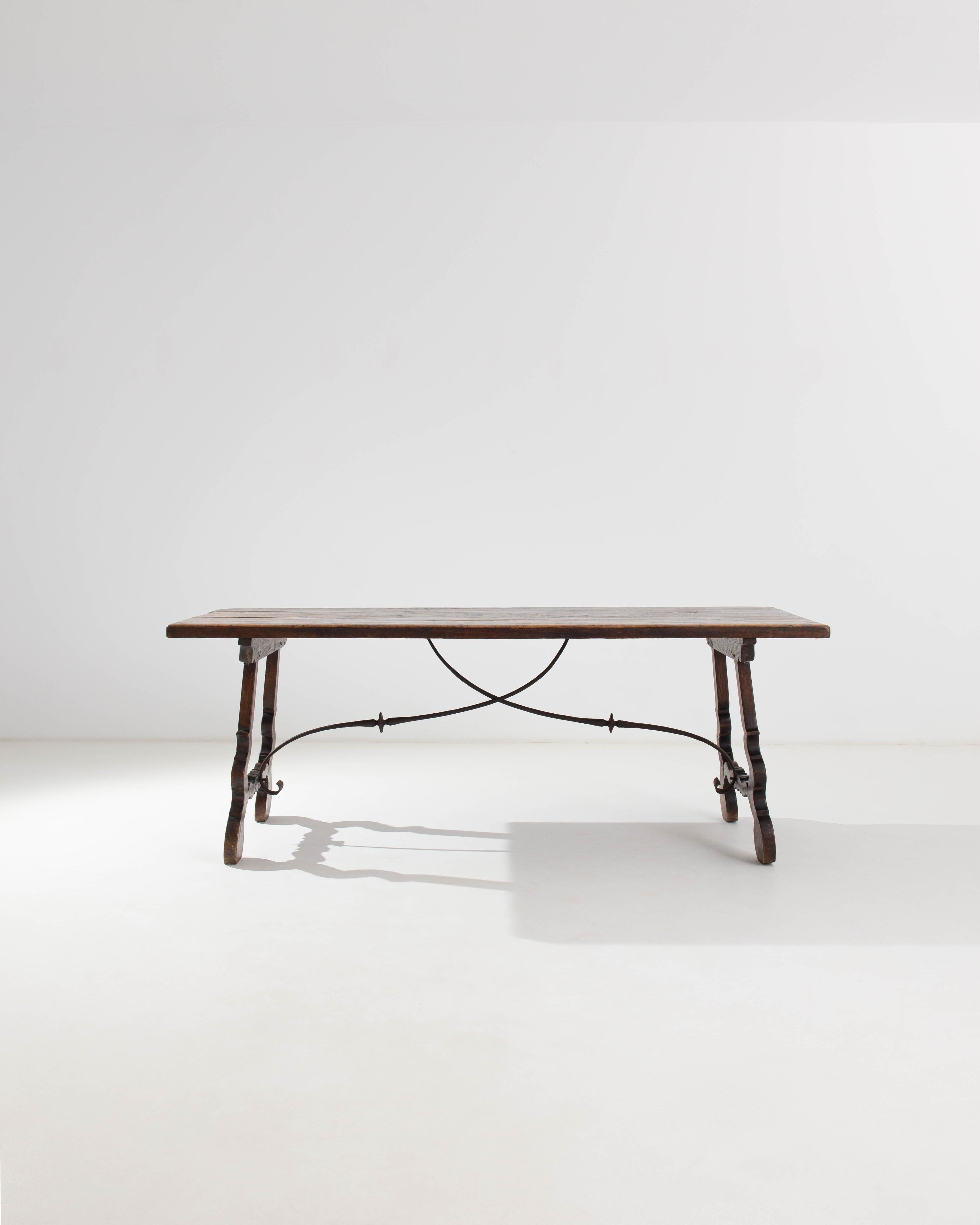 The design of this antique wooden dining table is handsome and poetic; the rich patina of the dark wood has a beauty all its own. Made in Spain in the 1800s, the form is an elegant interpretation of the trestle table, elevated by the intricate shape