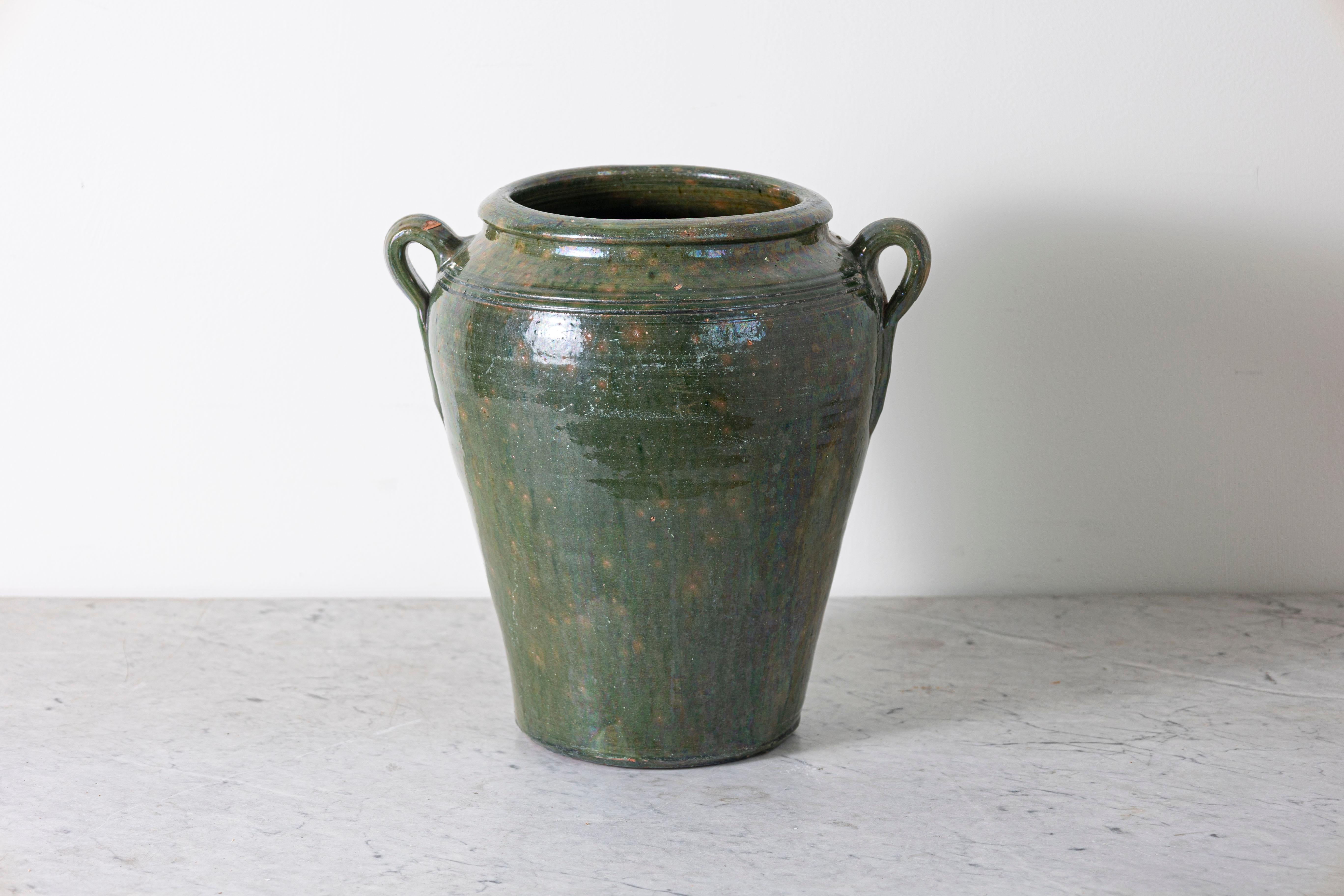 Questa giara in terracotta spagnola del XIX secolo presenta un'elegante silhouette ispirata all'anfora, ornata da due manici ad anello. La caratteristica smaltatura verde, applicata con precisione, conferisce al pezzo una finitura lucida e ne
