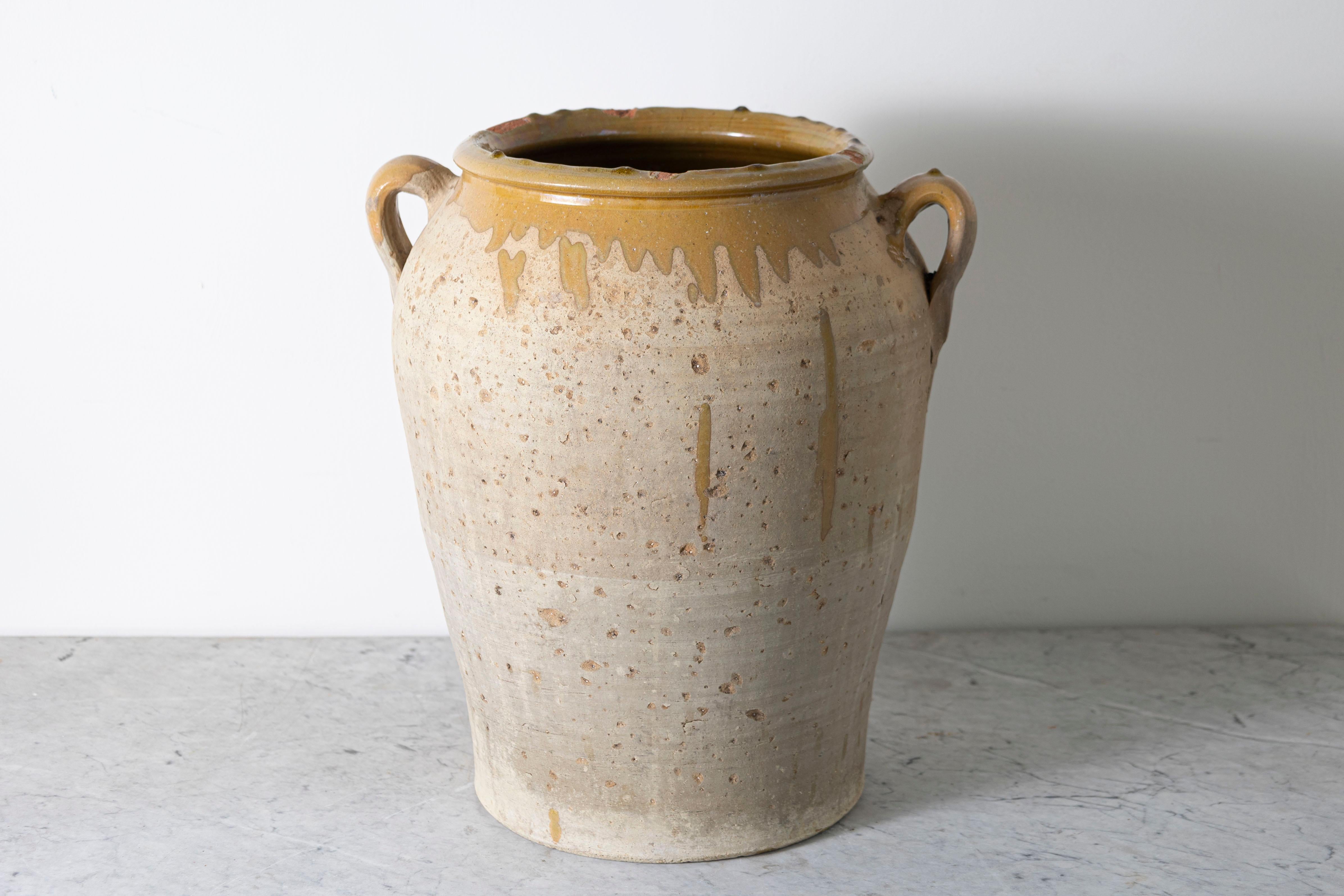 Questo vaso in ceramica spagnola del XIX secolo è un esempio di artigianato mediterraneo tradizionale. Realizzata in terracotta, la sua forma robusta e utilitaria è caratterizzata da una texture maculata e invecchiata che riflette il suo uso storico