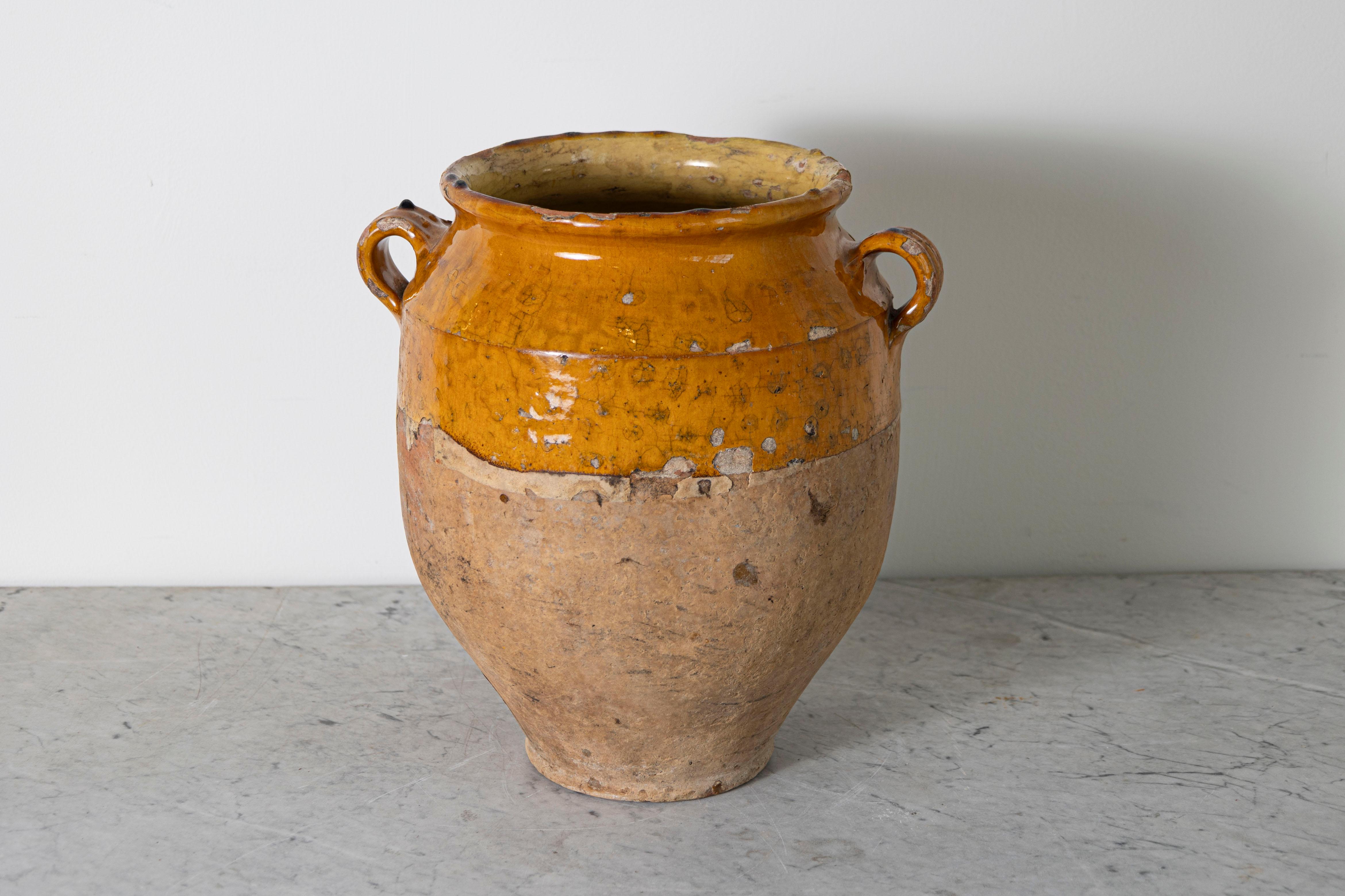 Questo vaso di ceramica spagnolo del XIX secolo è un bellissimo esempio di artigianato mediterraneo rustico. Realizzato a mano in terracotta, l'orcio presenta uno smalto ocra caldo sulla parte superiore, in contrasto con la base non smaltata e