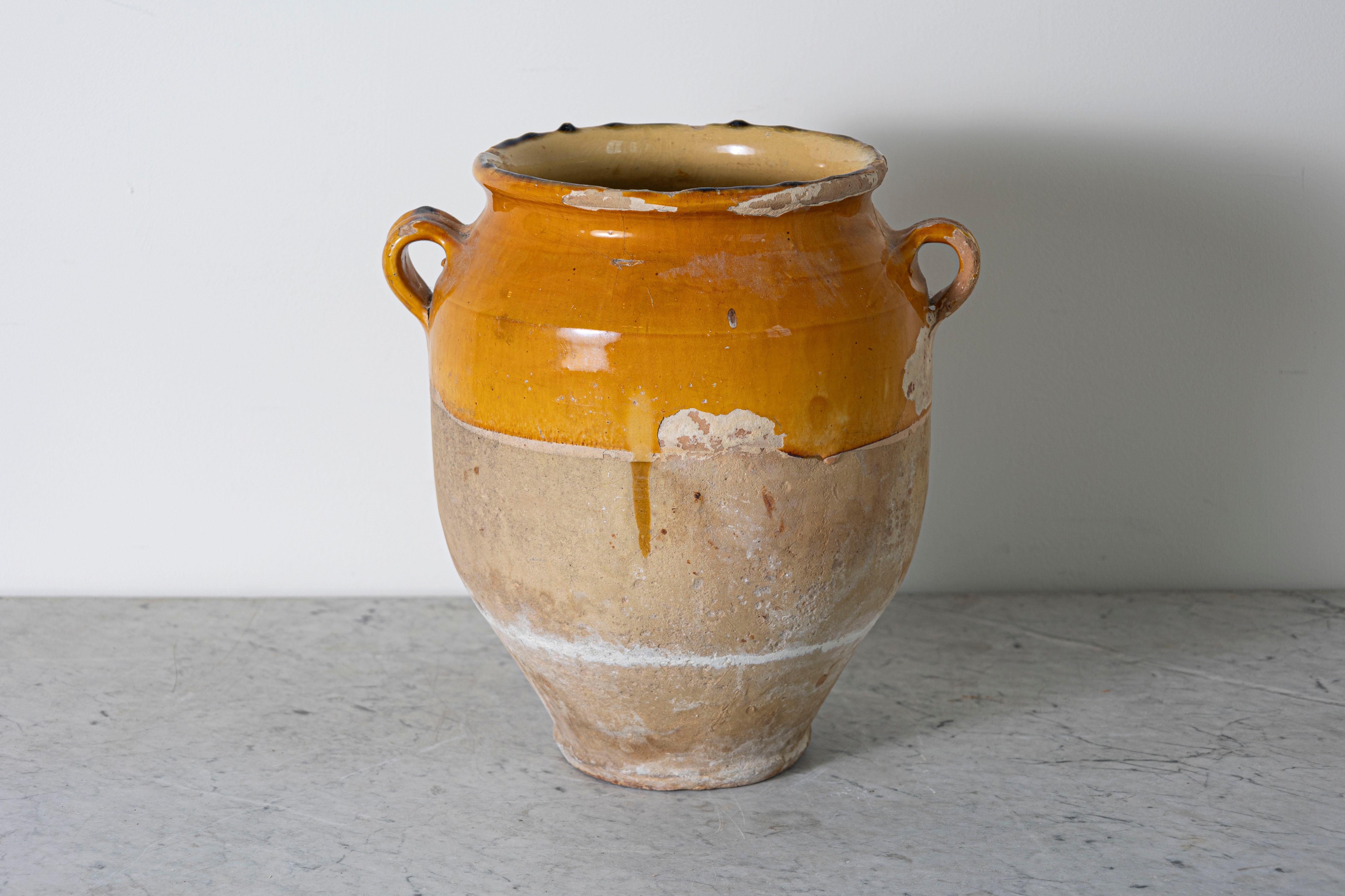 Questo vaso di ceramica spagnolo del XIX secolo è un bellissimo esempio di artigianato mediterraneo rustico. Realizzato a mano in terracotta, l'orcio presenta uno smalto ocra caldo sulla parte superiore, in contrasto con la base non smaltata e