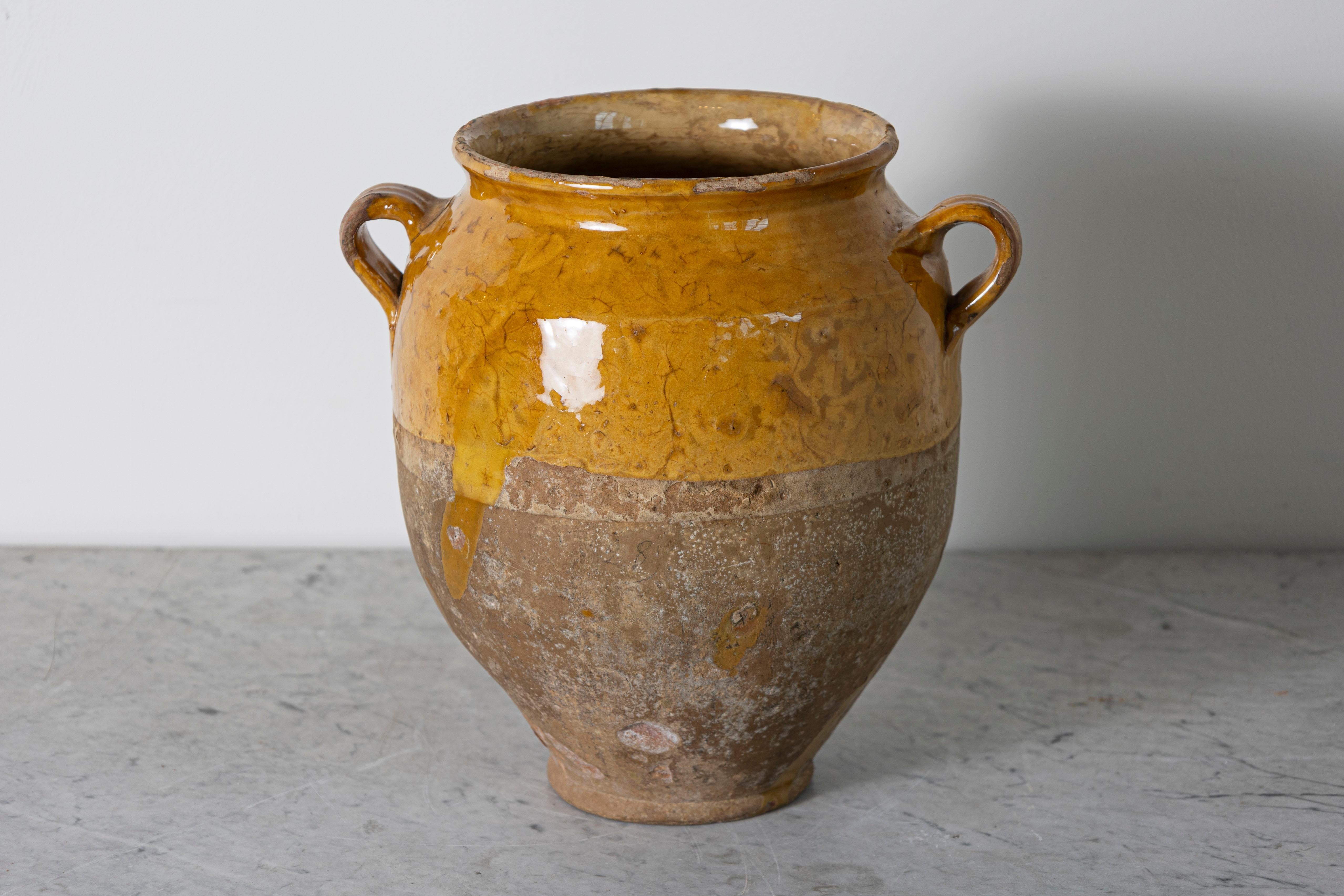 Questo vaso di ceramica spagnolo del XIX secolo è un bellissimo esempio di artigianato mediterraneo rustico. Realizzato a mano in terracotta, l'orcio presenta uno smalto ocra caldo sulla parte superiore, in contrasto con la base non smaltata e
