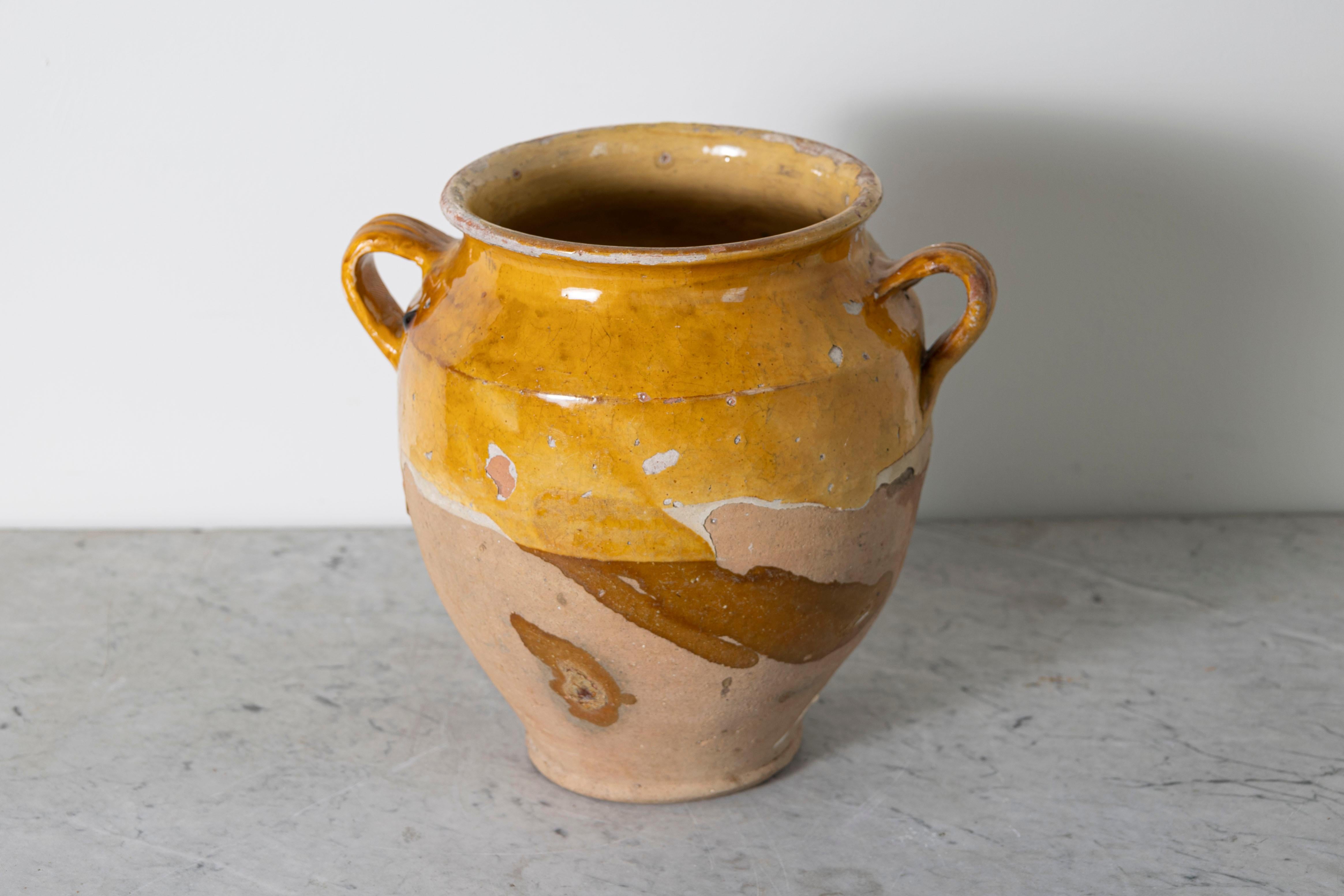 Questo vaso di ceramica spagnolo del XIX secolo è un bellissimo esempio di artigianato mediterraneo rustico. Realizzato a mano in terracotta, l'orcio presenta uno smalto ocra caldo sulla parte superiore, in contrasto con la base non smaltata e