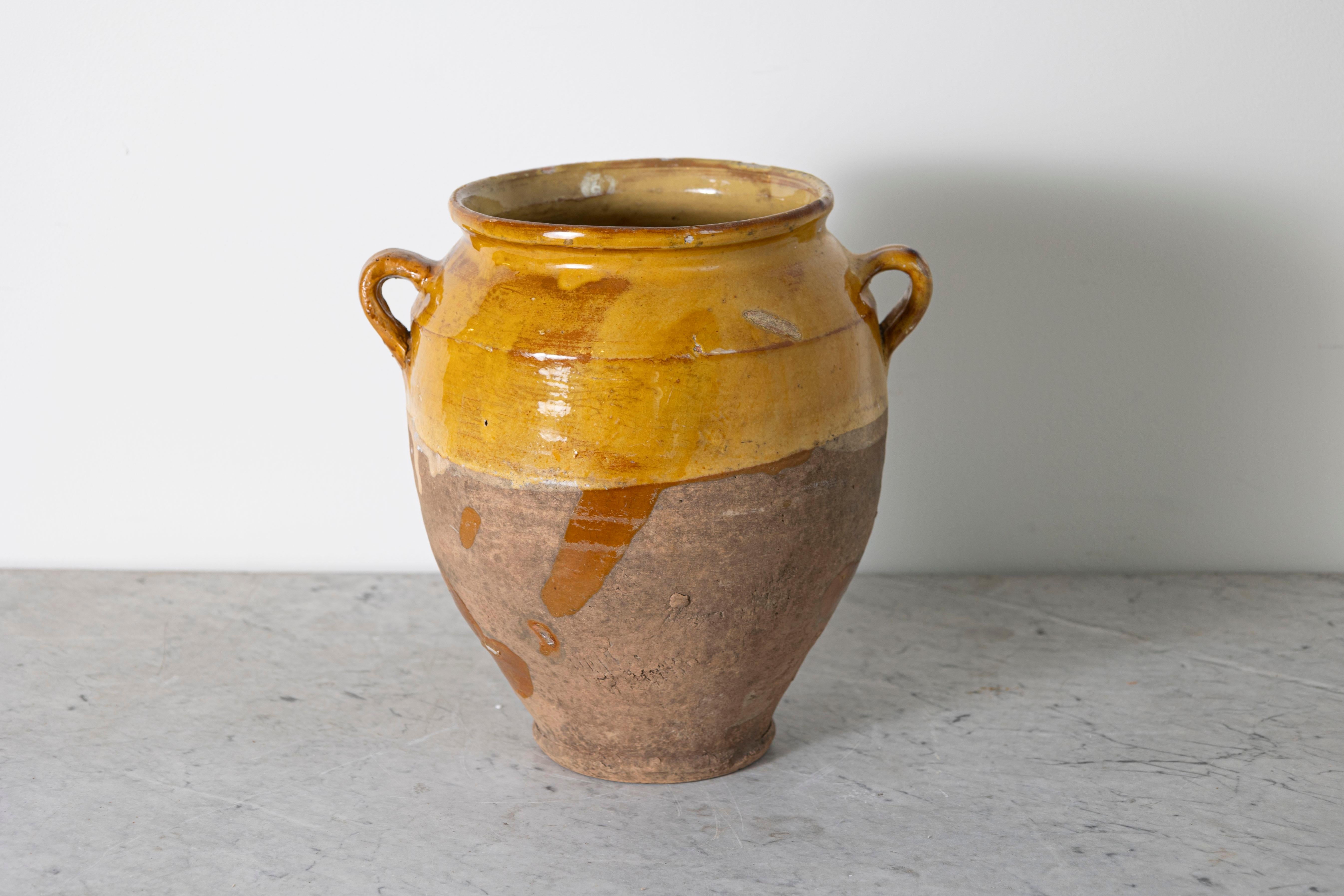 This 19th-century Spanish pottery jar is a beautiful example of rustic Mediterranean craftsmanship. Handcrafted from terracotta, the jar features a warm ochre glaze on the upper portion, contrasting with the unglazed, weathered base that highlights