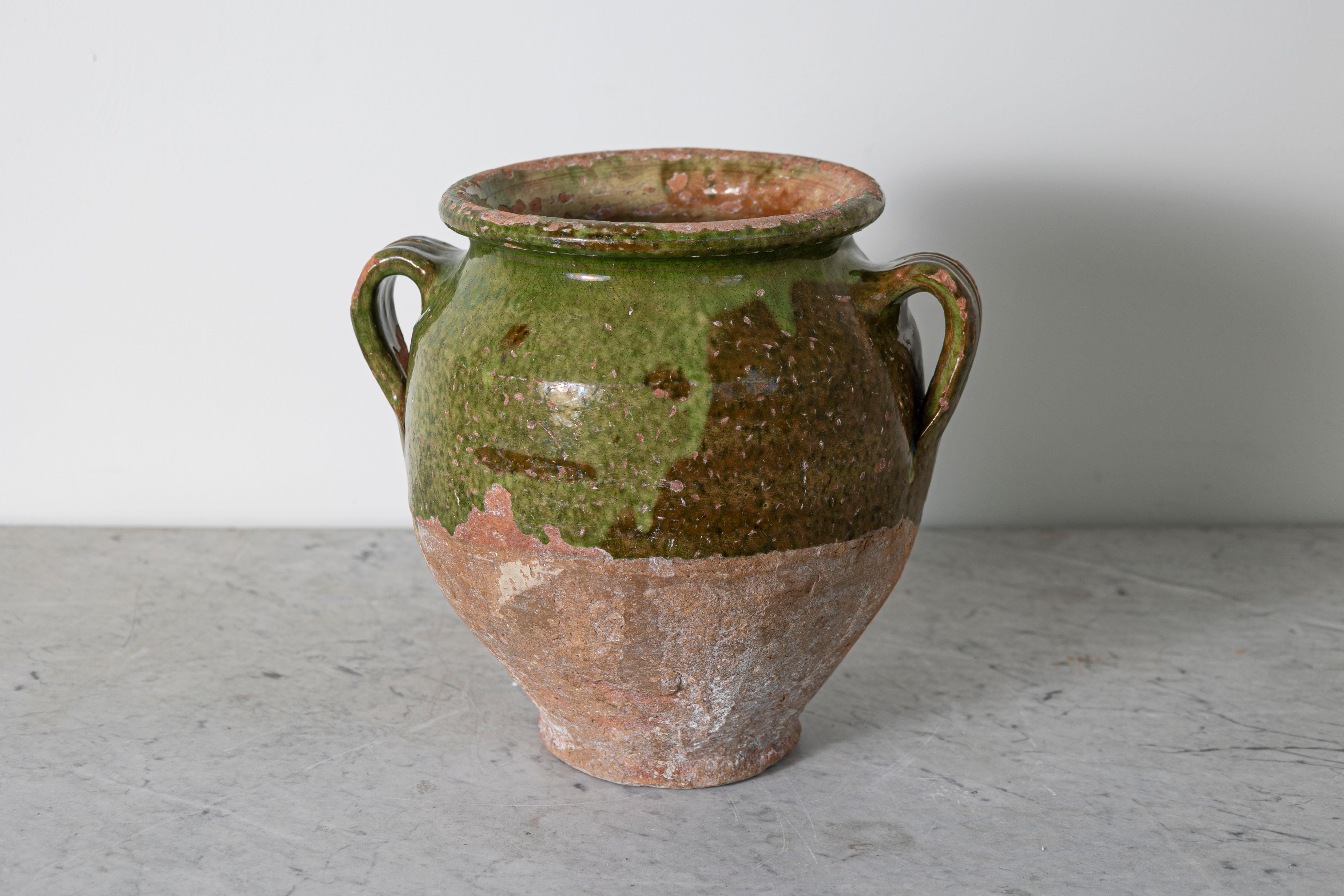 This 19th-century Spanish pottery jar showcases traditional craftsmanship and rustic charm. Handcrafted from terracotta, it features a vibrant green glaze on the upper portion, contrasting beautifully with the unglazed, weathered lower half. The
