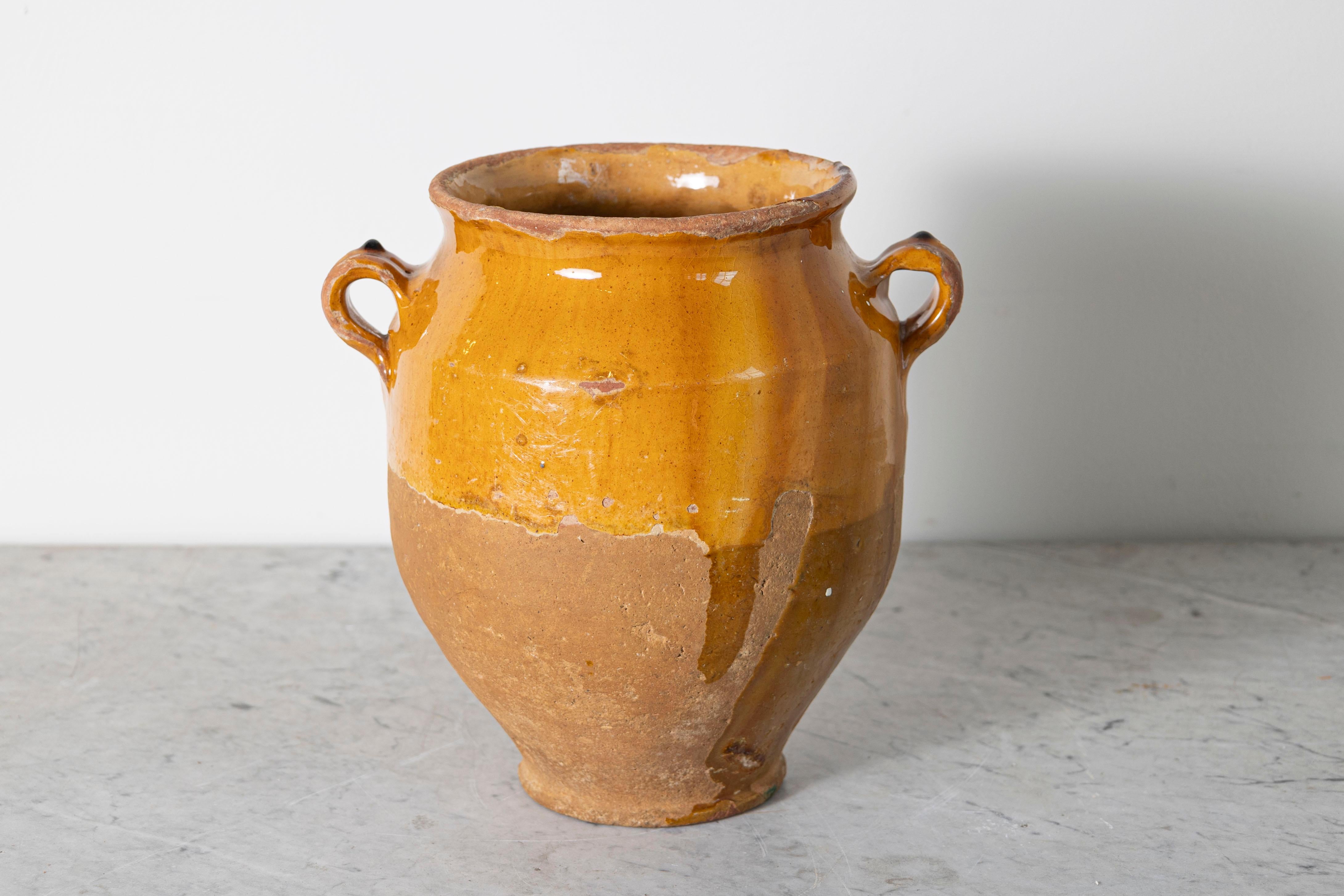 Questo vaso di ceramica spagnolo del XIX secolo è un bellissimo esempio di artigianato mediterraneo rustico. Realizzato a mano in terracotta, l'orcio presenta uno smalto ocra caldo sulla parte superiore, in contrasto con la base non smaltata e