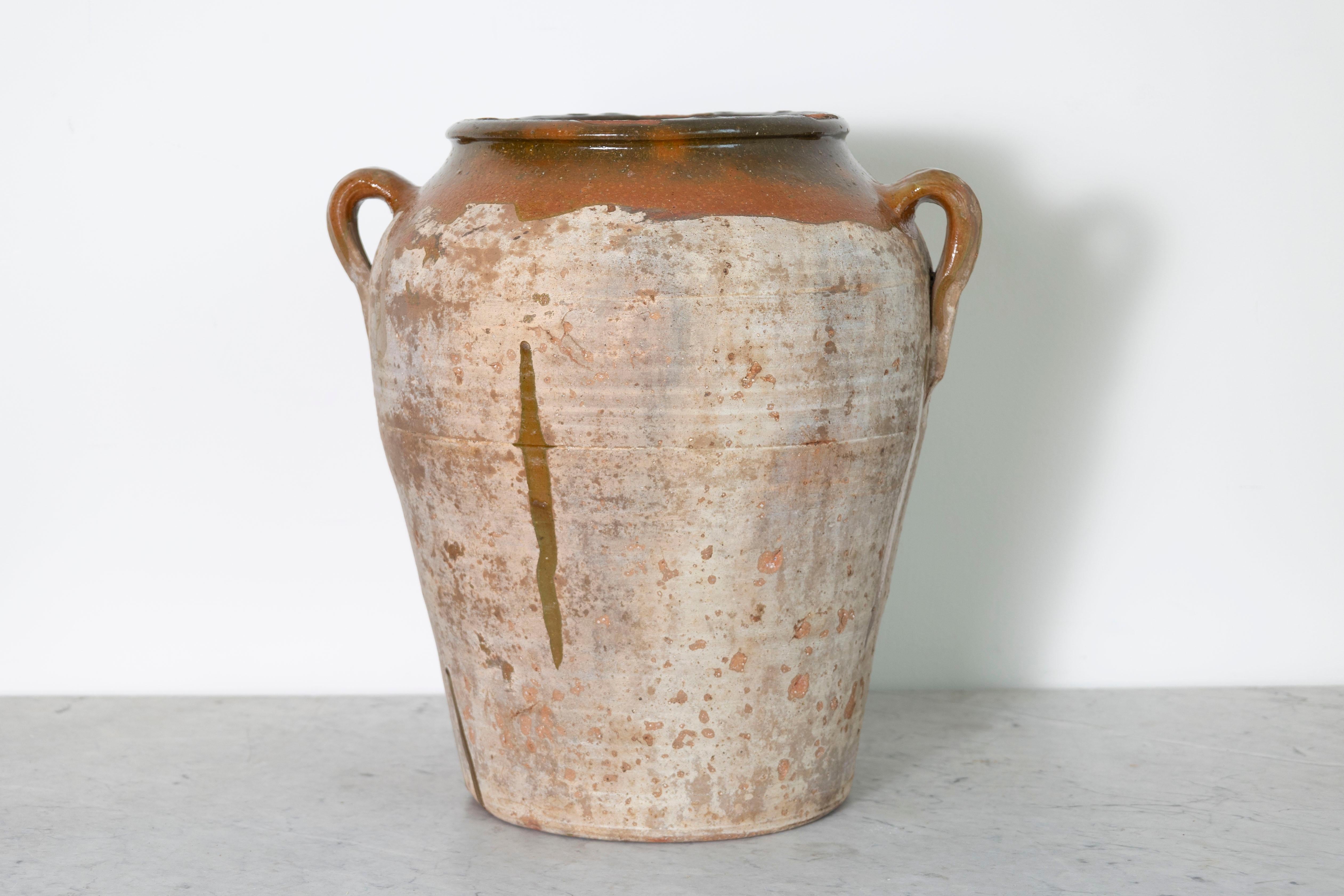 Questo vaso in terracotta spagnolo del XIX secolo è un notevole esempio di artigianato rustico, caratterizzato da una sobria eleganza con i suoi toni terrosi e la sua finitura strutturata. I doppi manici e l'apertura a bocca larga ne esaltano il