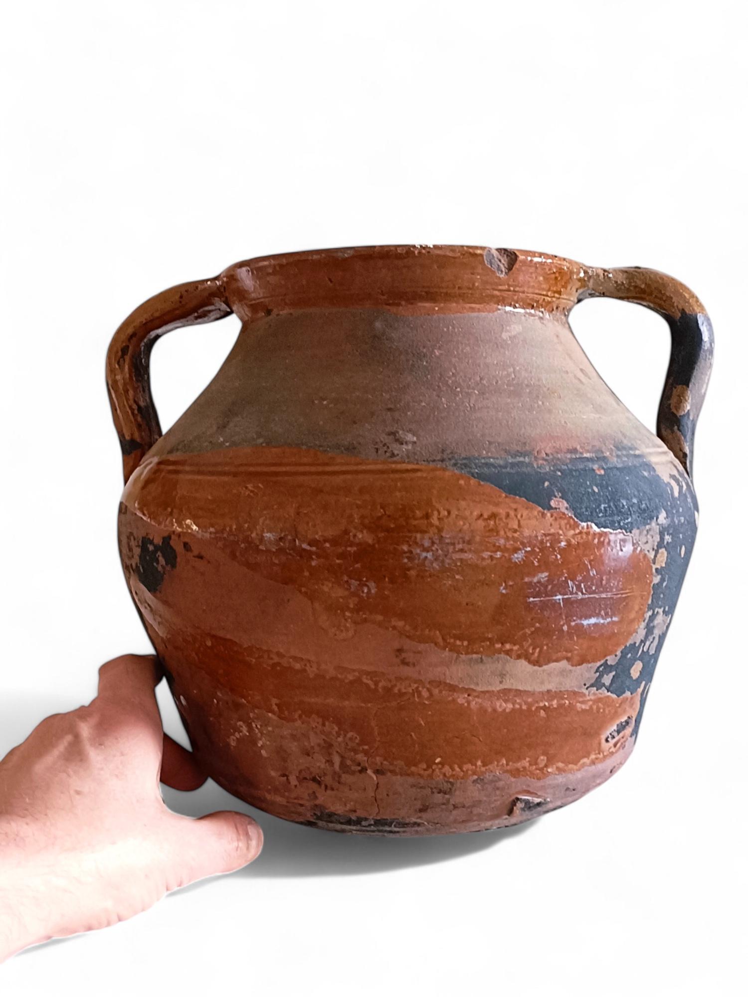 Un antico vaso di terracotta da cucina spagnolo di grandi dimensioni risalente al XIX secolo con una patina rovinata dagli agenti atmosferici. 

Questo tipo di ceramica è stata utilizzata in Europa per secoli per cucinare sul camino, posizionandola