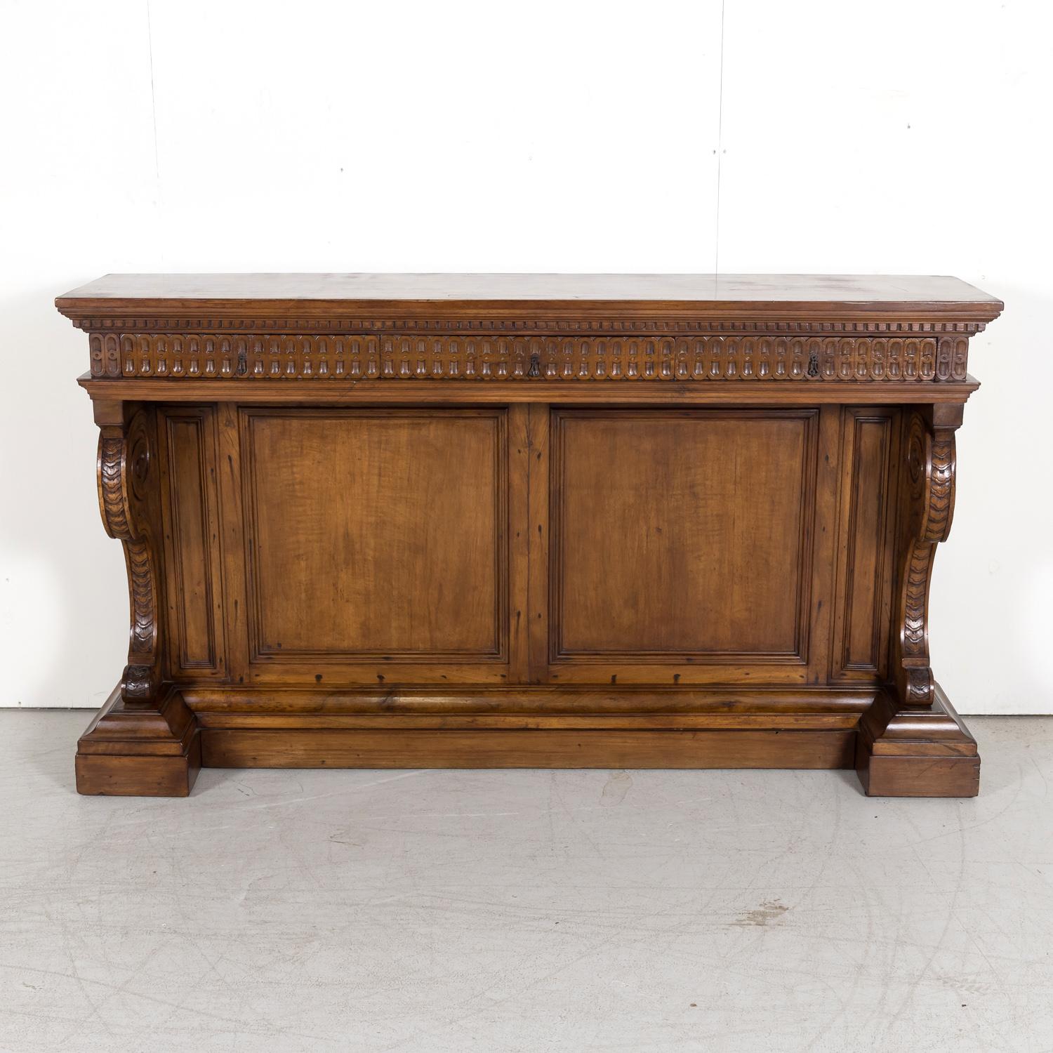 A handsome 19th Century Spanish Renaissance style carved walnut console from the Catalan region, circa 1890s, having a rectangular plank top above a frieze with dentil molding over three drawers with original iron drop handles. Below is molded panel