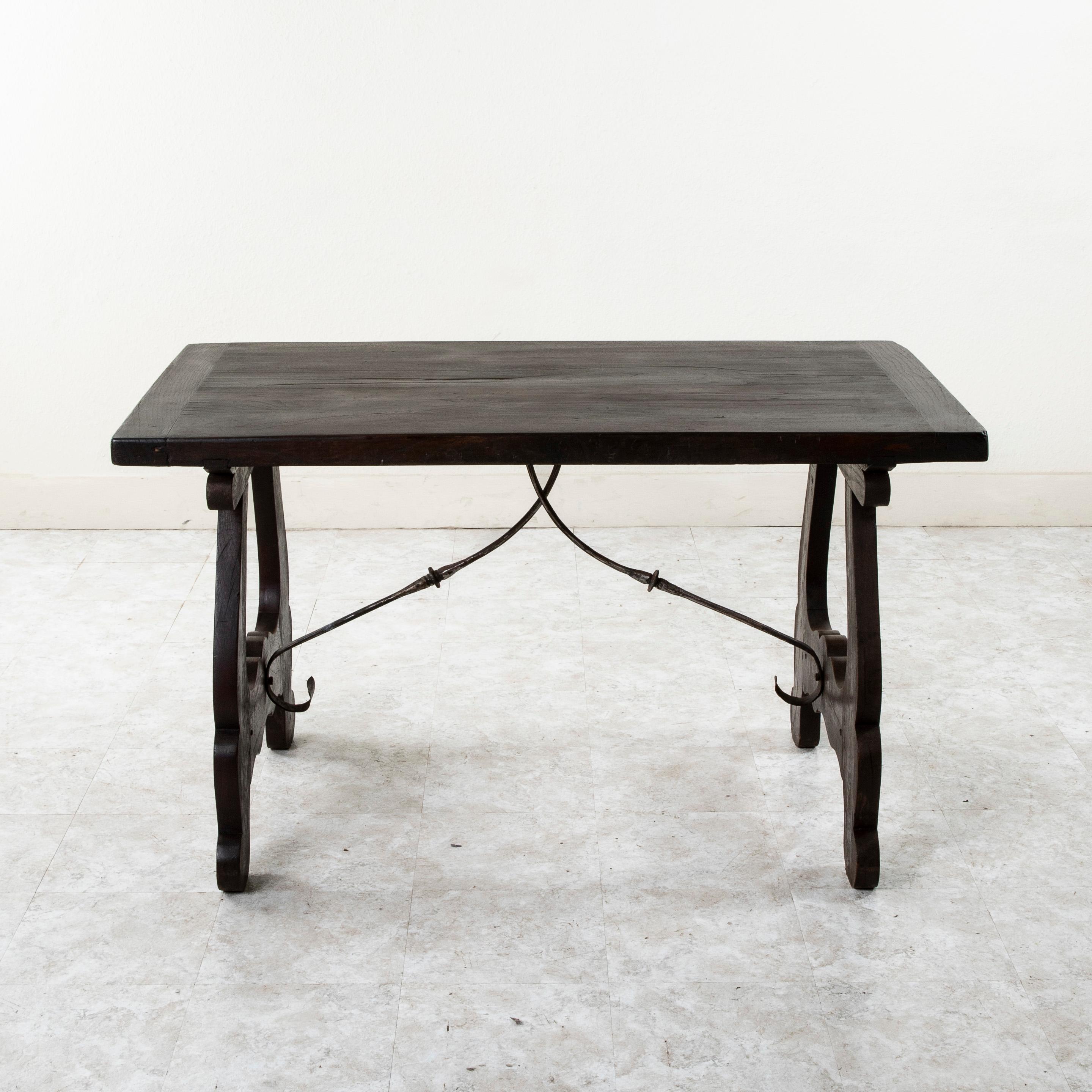 This small scale late nineteenth century Spanish Renaissance style table features a 29-inch wide oak top joined to its elegantly curved legs by means of two splines that run the entire width of the table. Hand forged iron supports connecting the