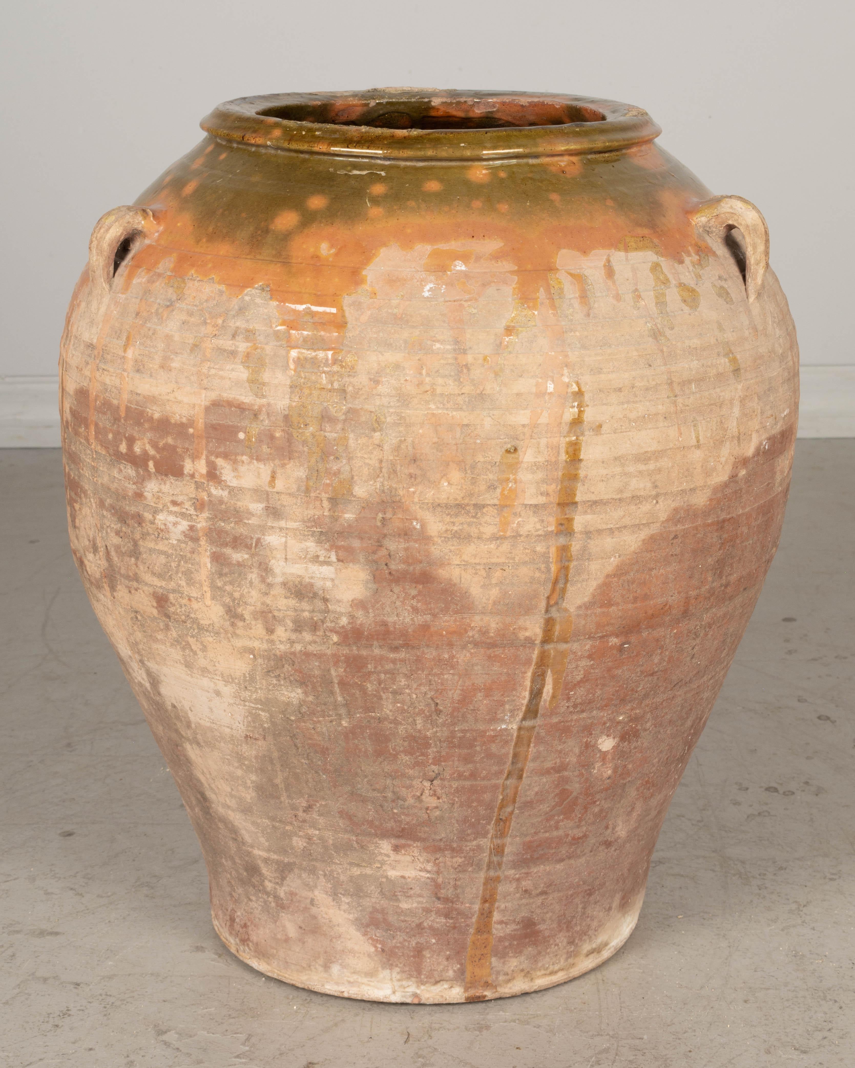 A large 19th century Spanish terracotta olive jar with orange and green glaze at the rim dripping down the sides. Beautiful warm weathered patina. One of the small handles has broken off. Minor losses. Nice as a decorative piece for use indoors or