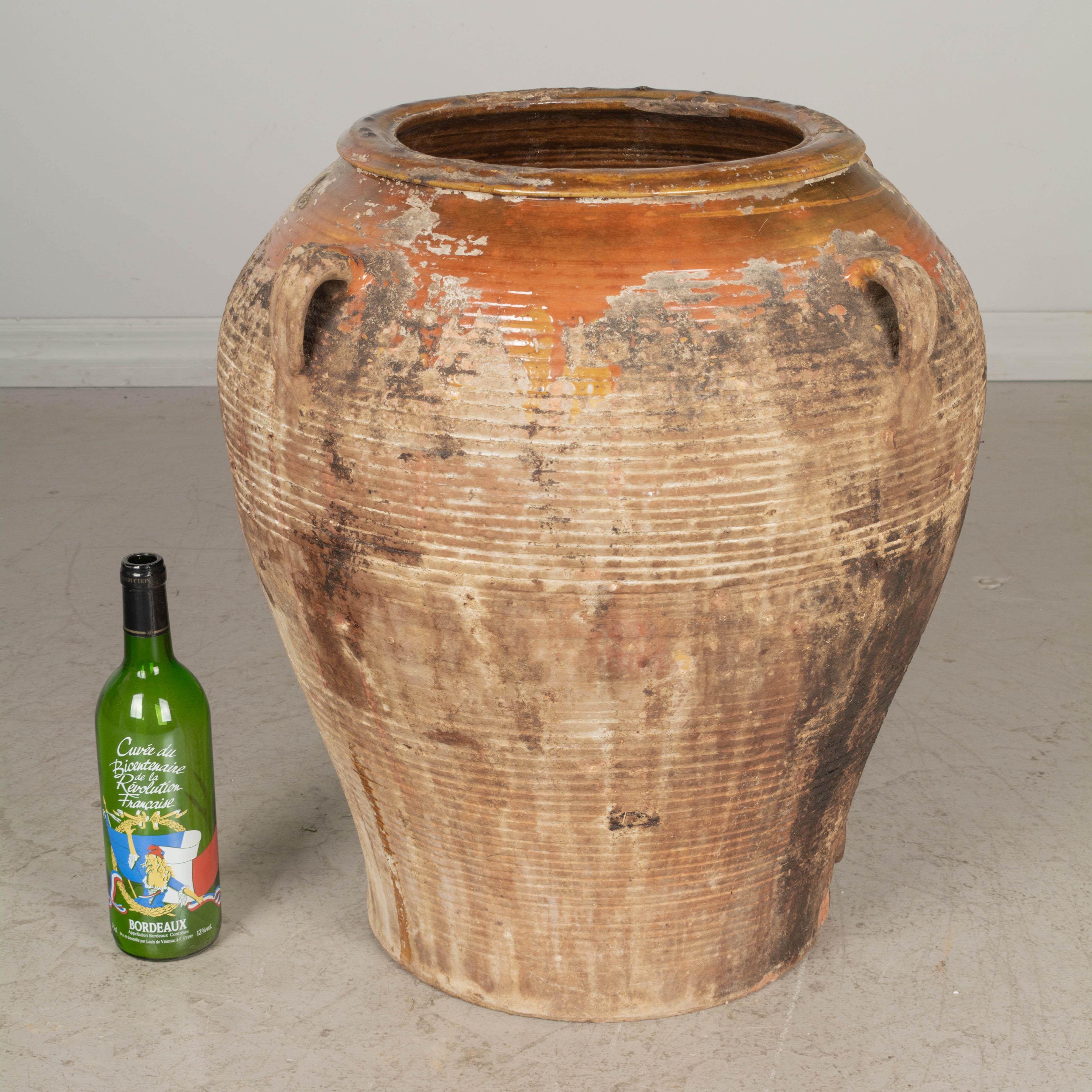 A large 19th century Spanish terracotta olive jar with orange yellow and green glaze at the rim dripping down the sides. Heavy oil residue has blackened over time creating an interesting patina. Dirt at the top has been left as is, but may be