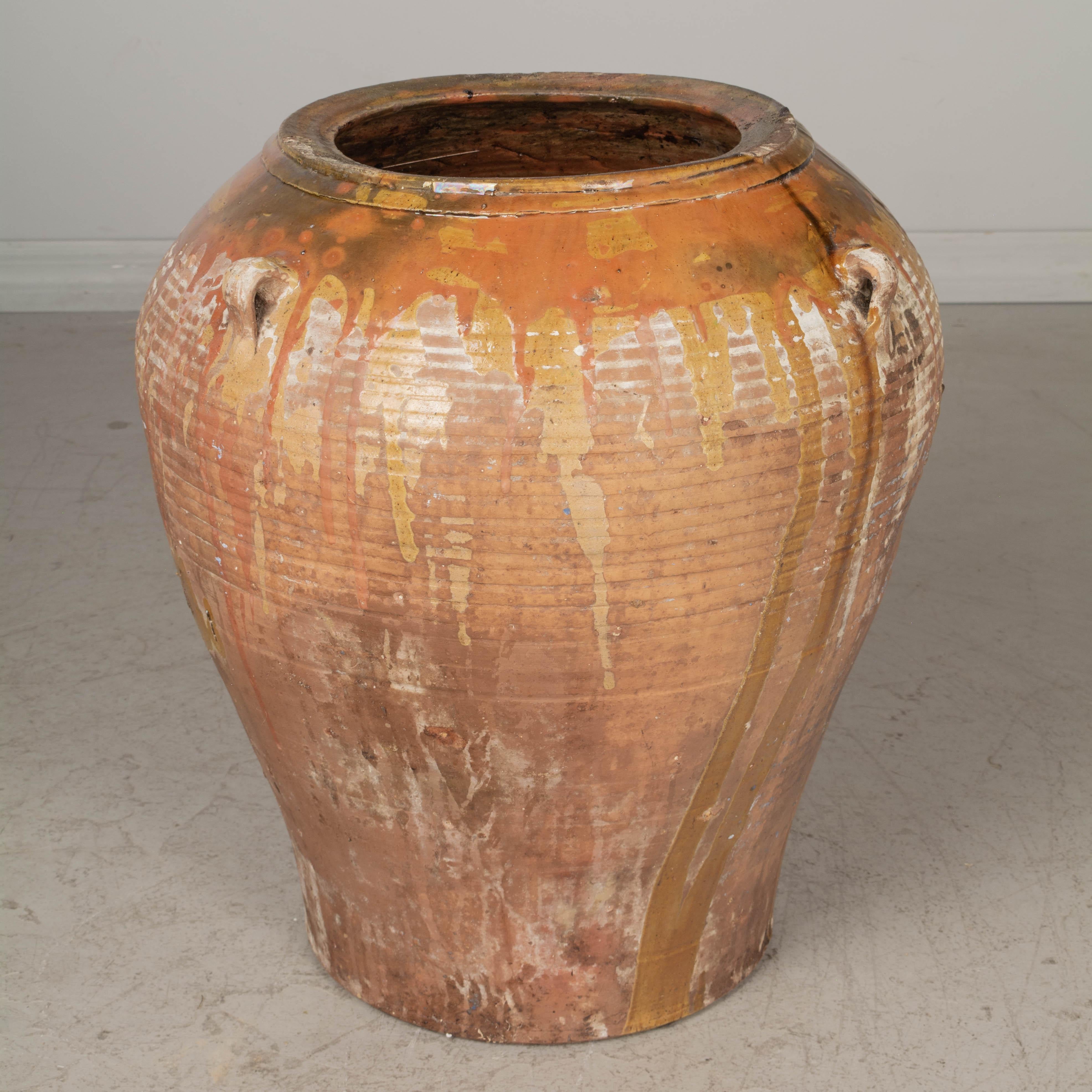 A large 19th century Spanish terracotta olive jar with orange, yellow and green glaze at the rim dripping down the sides. Three small handles. Old weathered patina. Minor losses. Nice as a decorative piece for use indoors or on a terrace. Large
