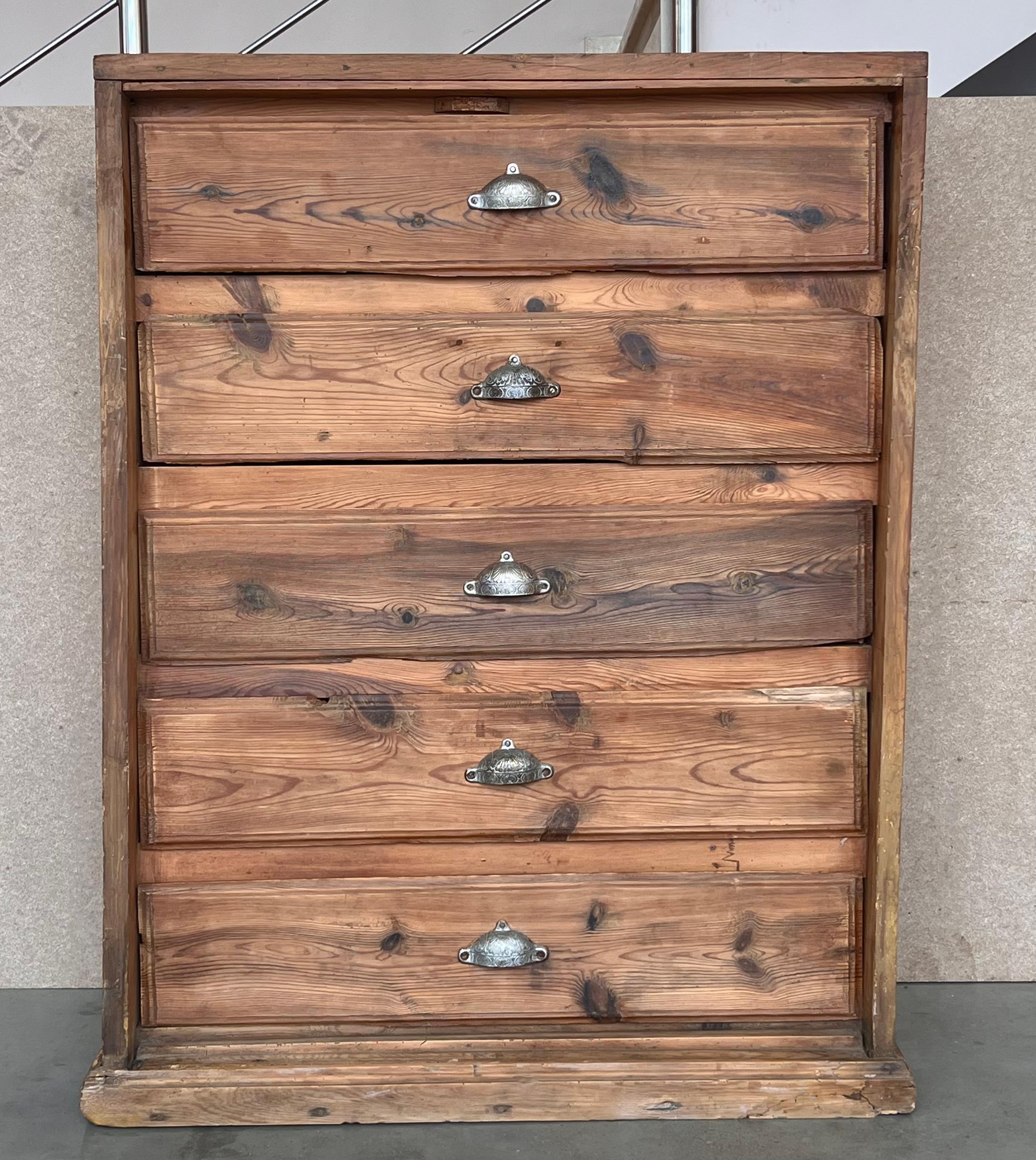 Una bella cassettiera alta in pino con piano d'appoggio a forma di piedistallo, seguito da cinque cassetti con placchette nichelate. Il cassetto superiore e quello inferiore hanno un profilo sagomato, mentre la sezione centrale è fiancheggiata da