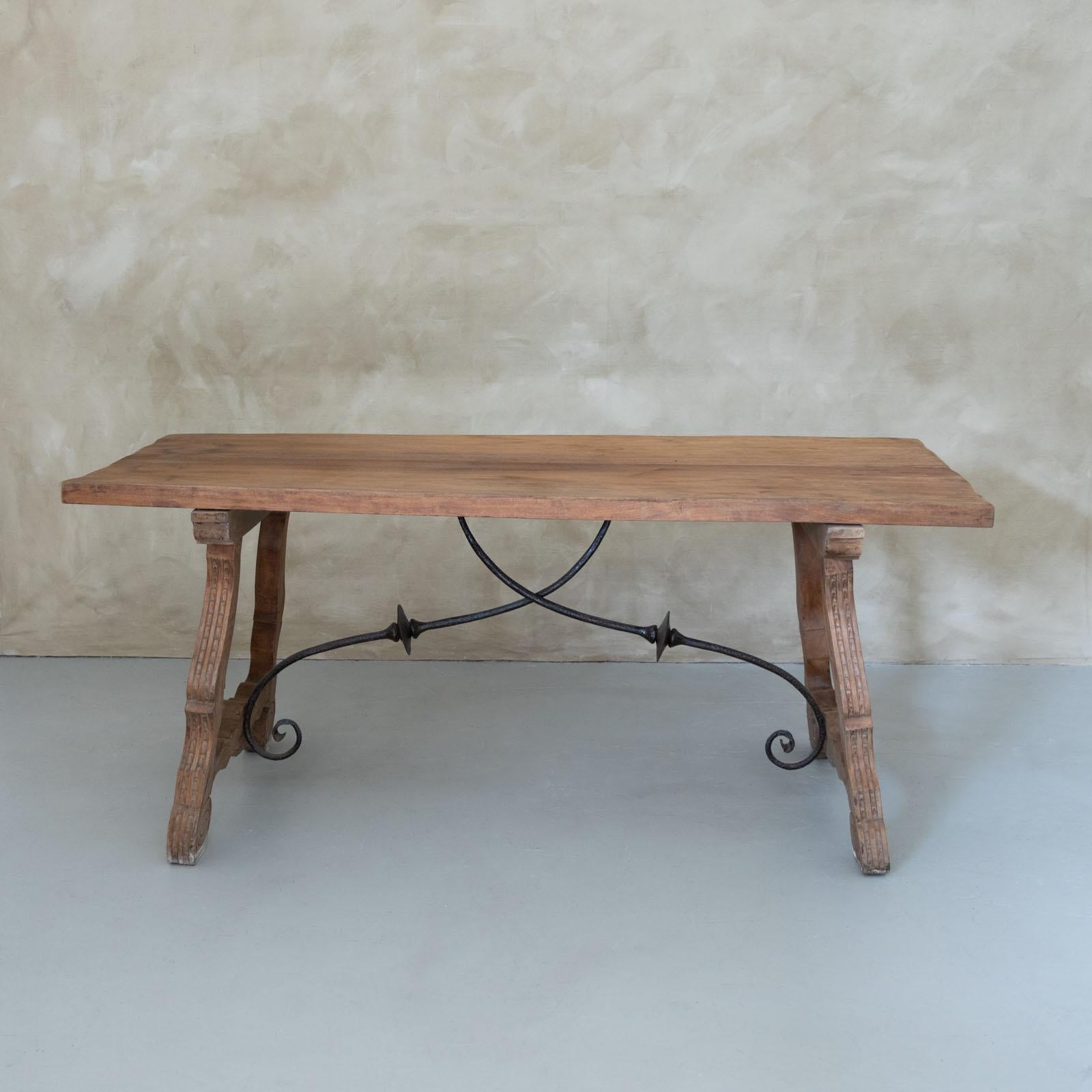 Beautiful 19th century wood trestle table from Spain. Rectangular top, four carved wood legs, and beautiful wrought iron detail beneath. Lovely scroll detail carved into each foot. Original finish shows nice age and patina. Perfect as library table,
