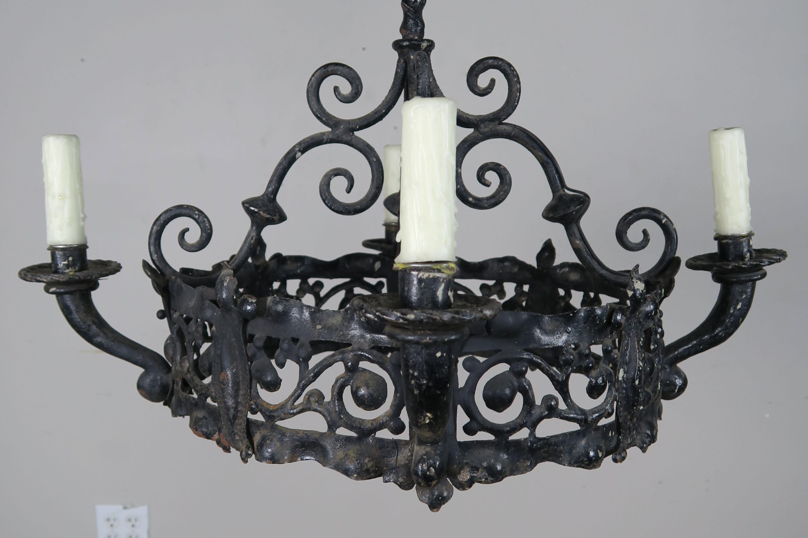 19th century Spanish 4-light wrought iron chandelier with intricate designs of scrolls and fleur-de-lis. The fixture was originally made for candles but has recently been wired for electricity. Cream drip wax candle covers.