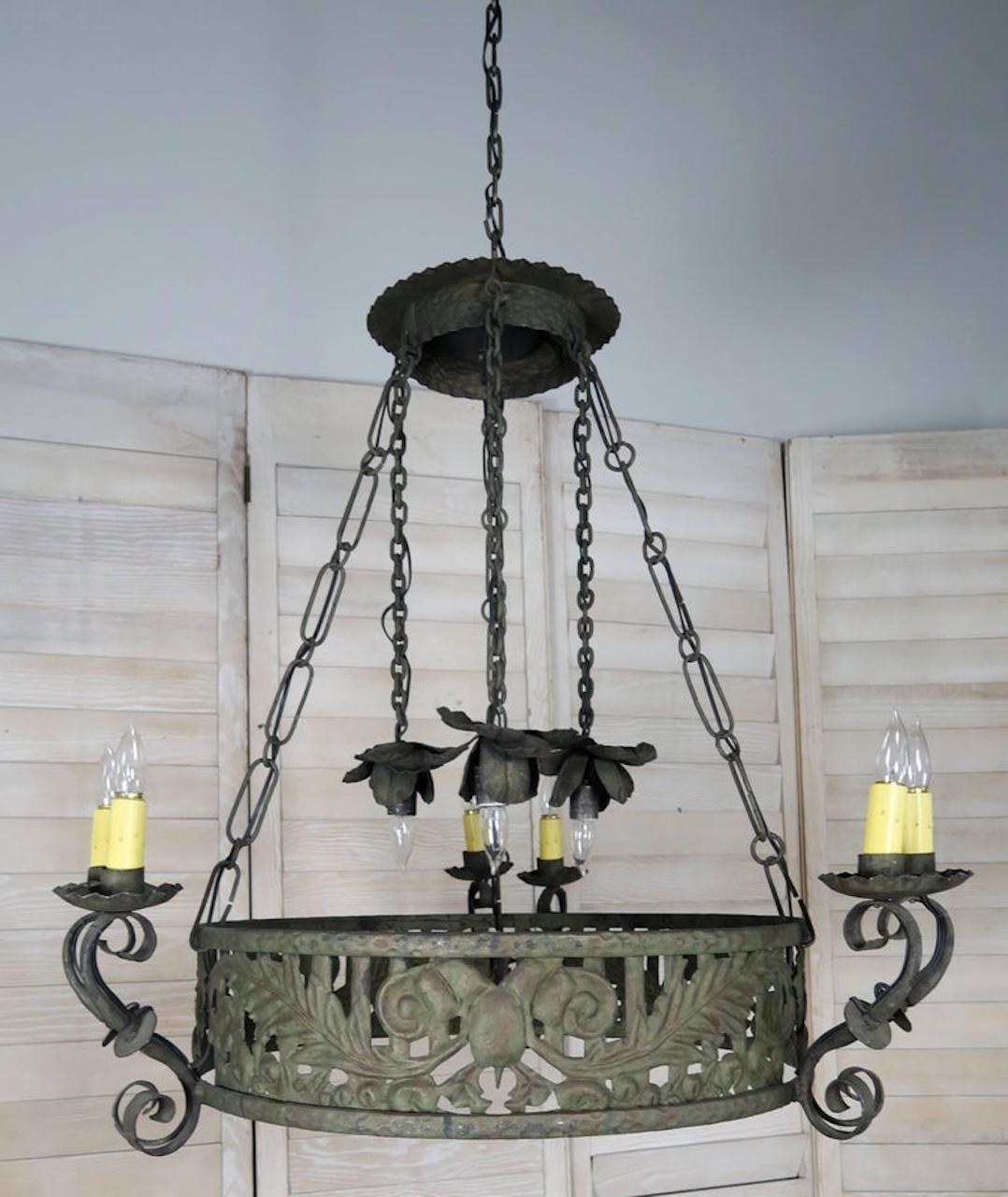 Lampadario circolare in ferro battuto del XIX secolo. Sei luci in tre coppie di due con coperchi di candele di cera a goccia sostenute da bracci a forma di voluta. Tre luci sospese al baldacchino da catene in ferro battuto sostengono tre grandi