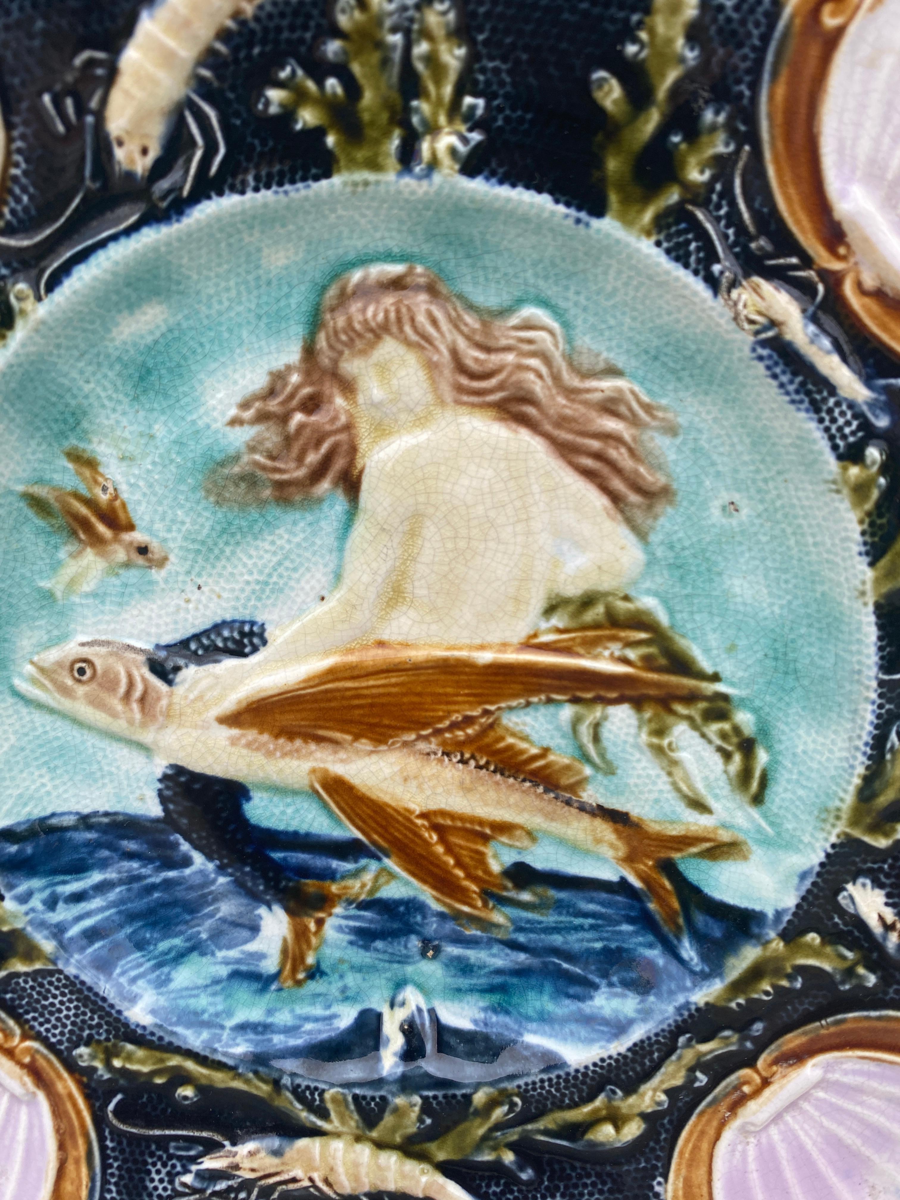 Square Majolica mermaid plate with shells on the corners, the mermaid sit on a flying fish, the border is decorated with shrimps, circa 1880.