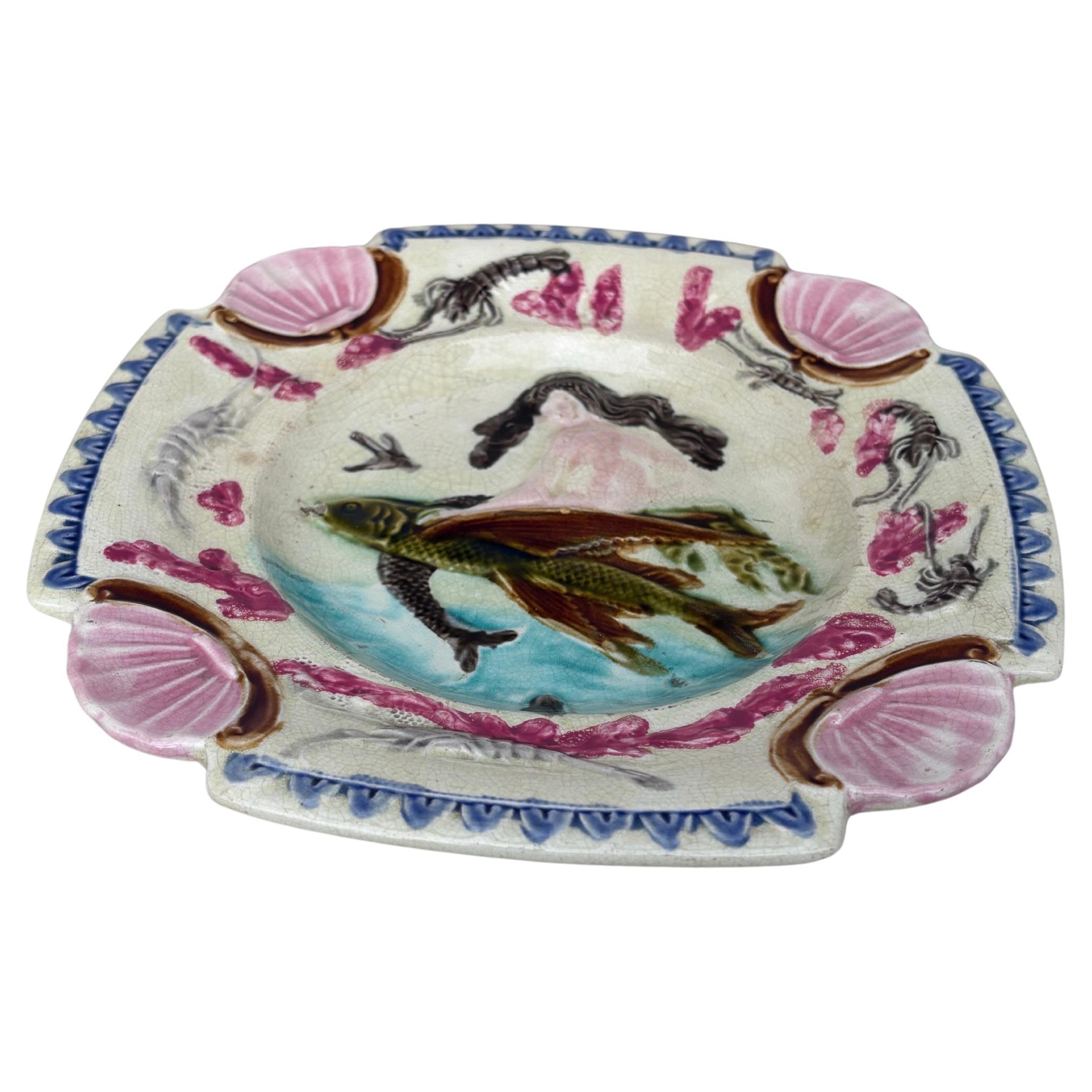 Quadratischer Majolika-Nixenteller mit Muscheln an den Ecken, die Meerjungfrau sitzt auf einem fliegenden Fisch, der Rand ist mit Krabben verziert, um 1880.