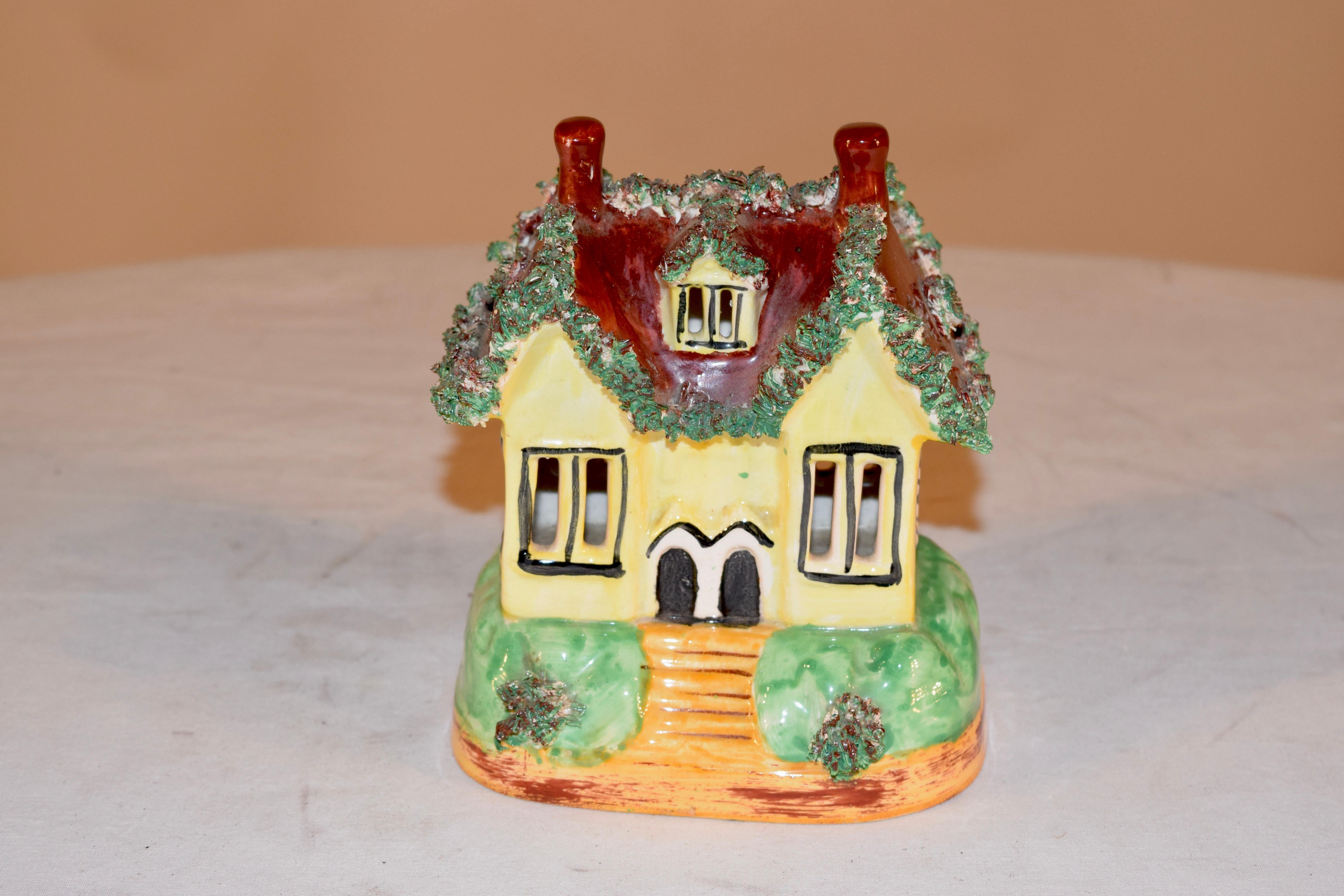 19th century Staffordshire cottage from England with flocking accents along the roofline, which is brown atop a cheery yellow cottage resting on a green base, which also has flocked accents.