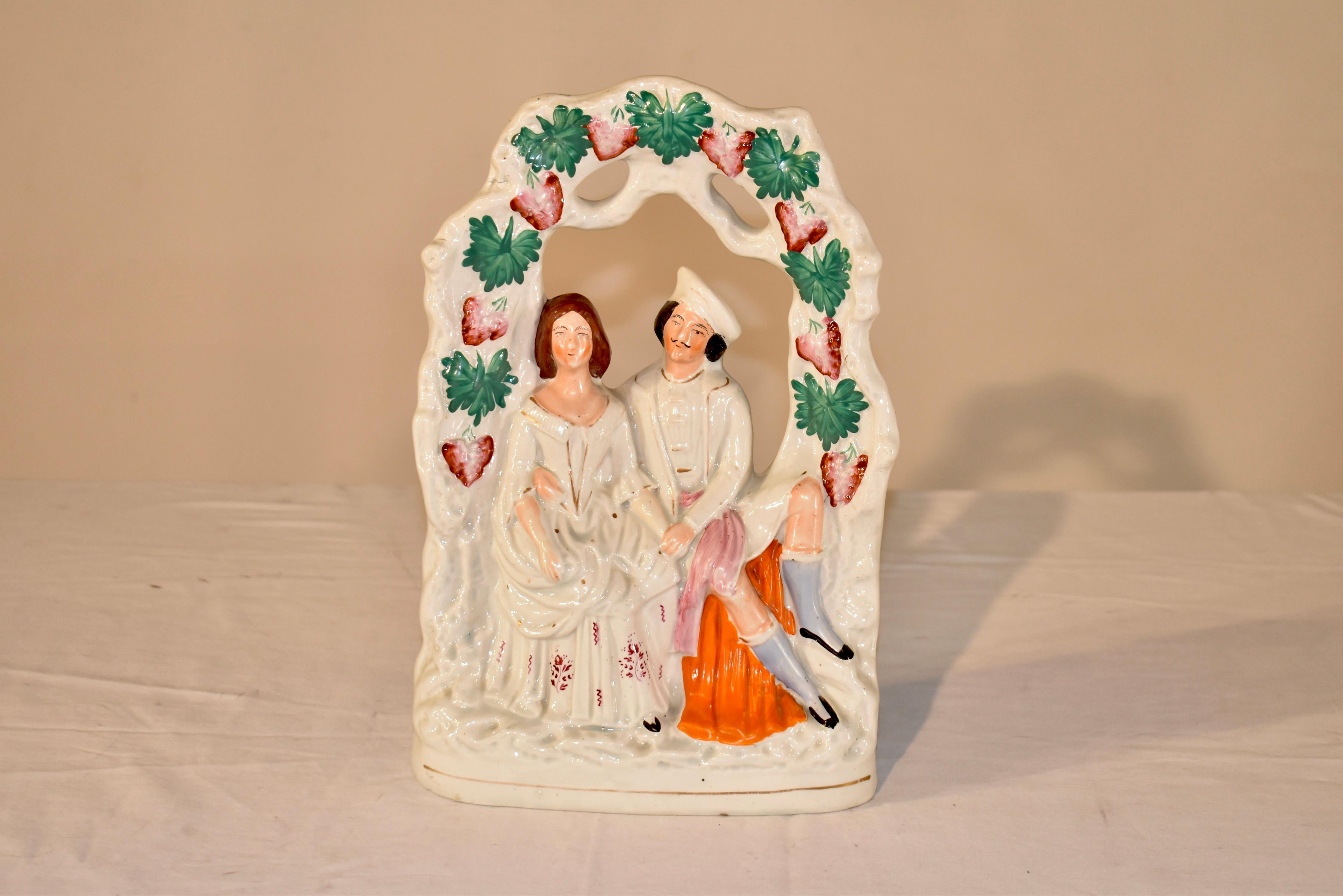 19th century Staffordshire figure group of a couple who appear to be courting sitting on a bench under an arbor with leaves and groups of flowers. The couple appears to be sitting holding hands and with his arm encircling her. They look as if they