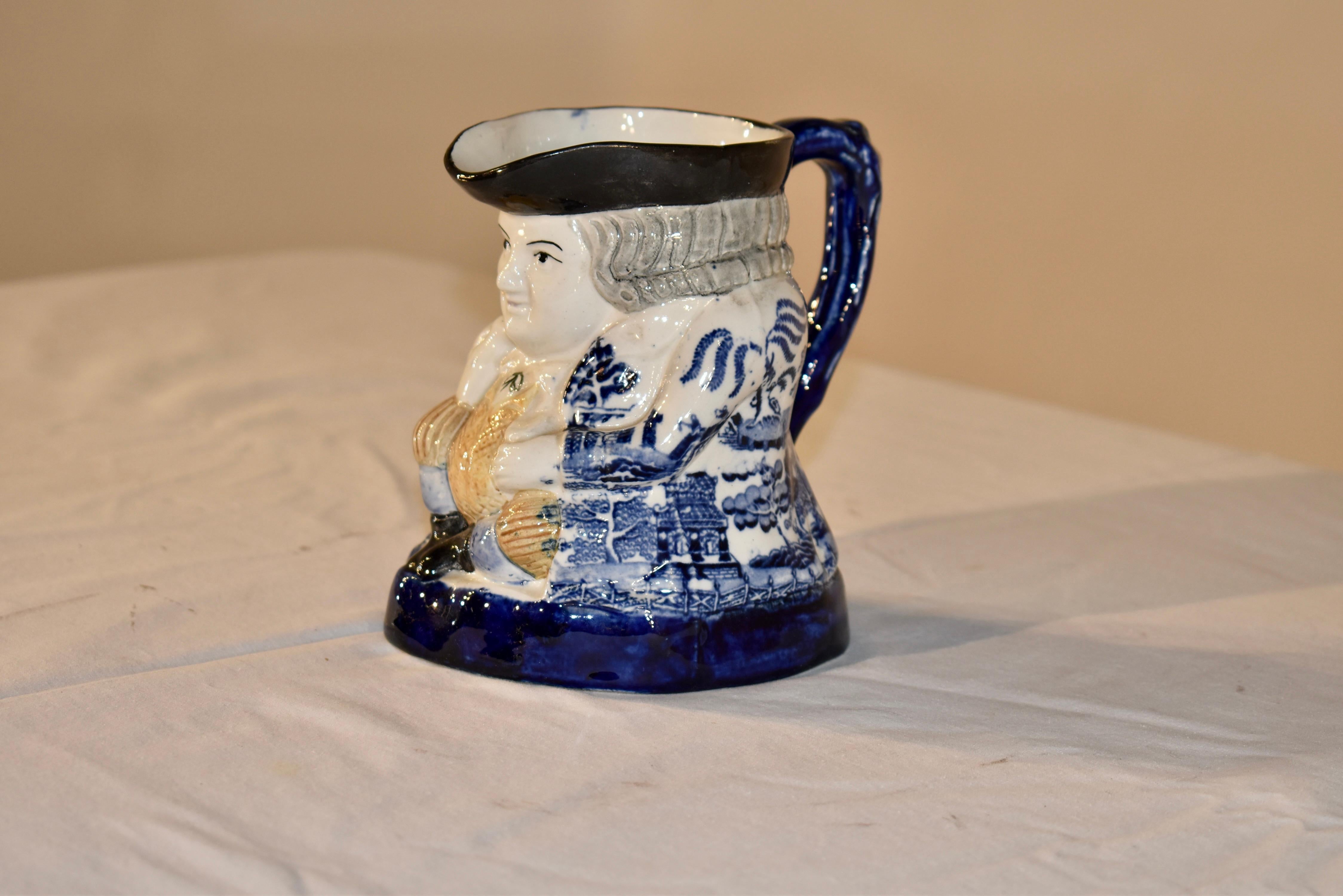 Lovely and unusual 19th century toby jug from the region of Staffordshire in England. The jug depicts a man, sitting with feet crossed and a black hat and a marvelous coat with the highly collectable Blue Willow pattern. The jug has a blue base and