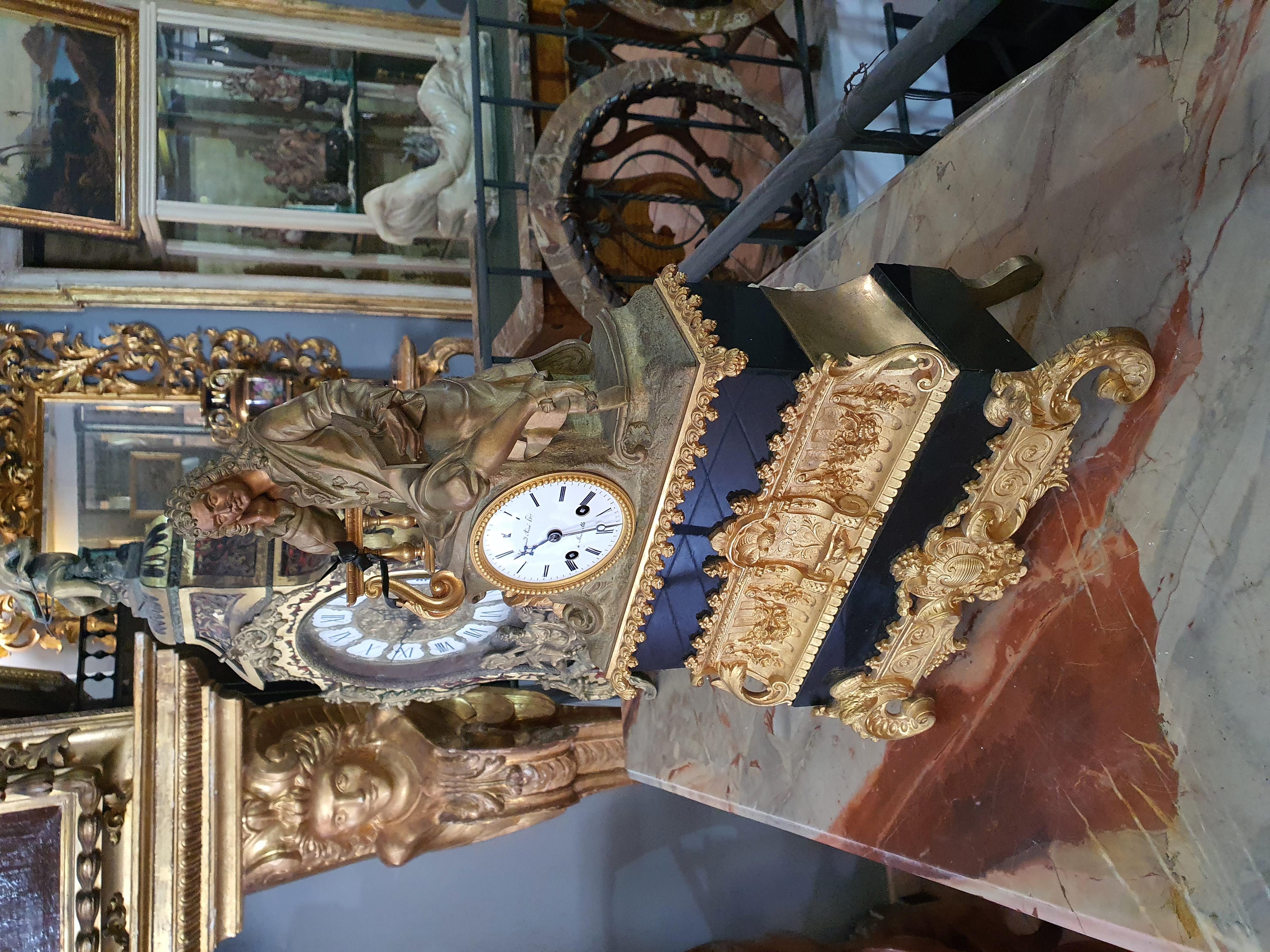 Horloge composée d'une structure à plusieurs ordres, alternant marbre noir et bronze doré, au sommet de laquelle se trouve la sculpture en bronze patiné d'un homme plongé dans la lecture, probablement Voltaire. Cadran en émail blanc, chiffres arabes