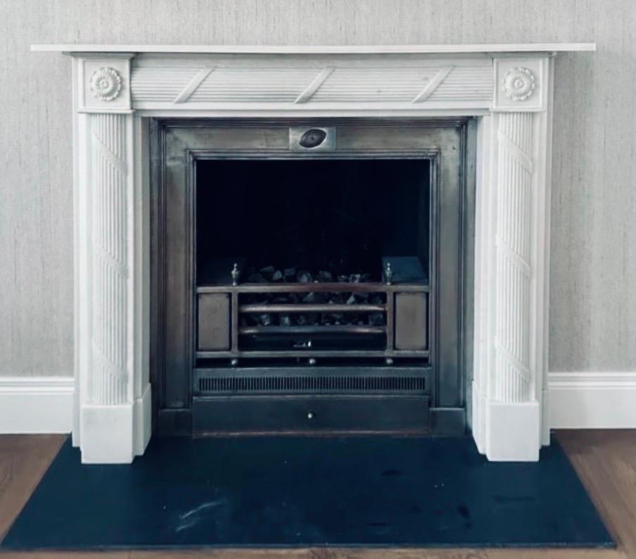 A well balanced medium sized 19th century Regency style hand carved statuary marble fireplace surround, a reeded top shelf sits directly above a stepped frieze with carved ribbon and reeding, flanked by framed high relief circular pateraes to the