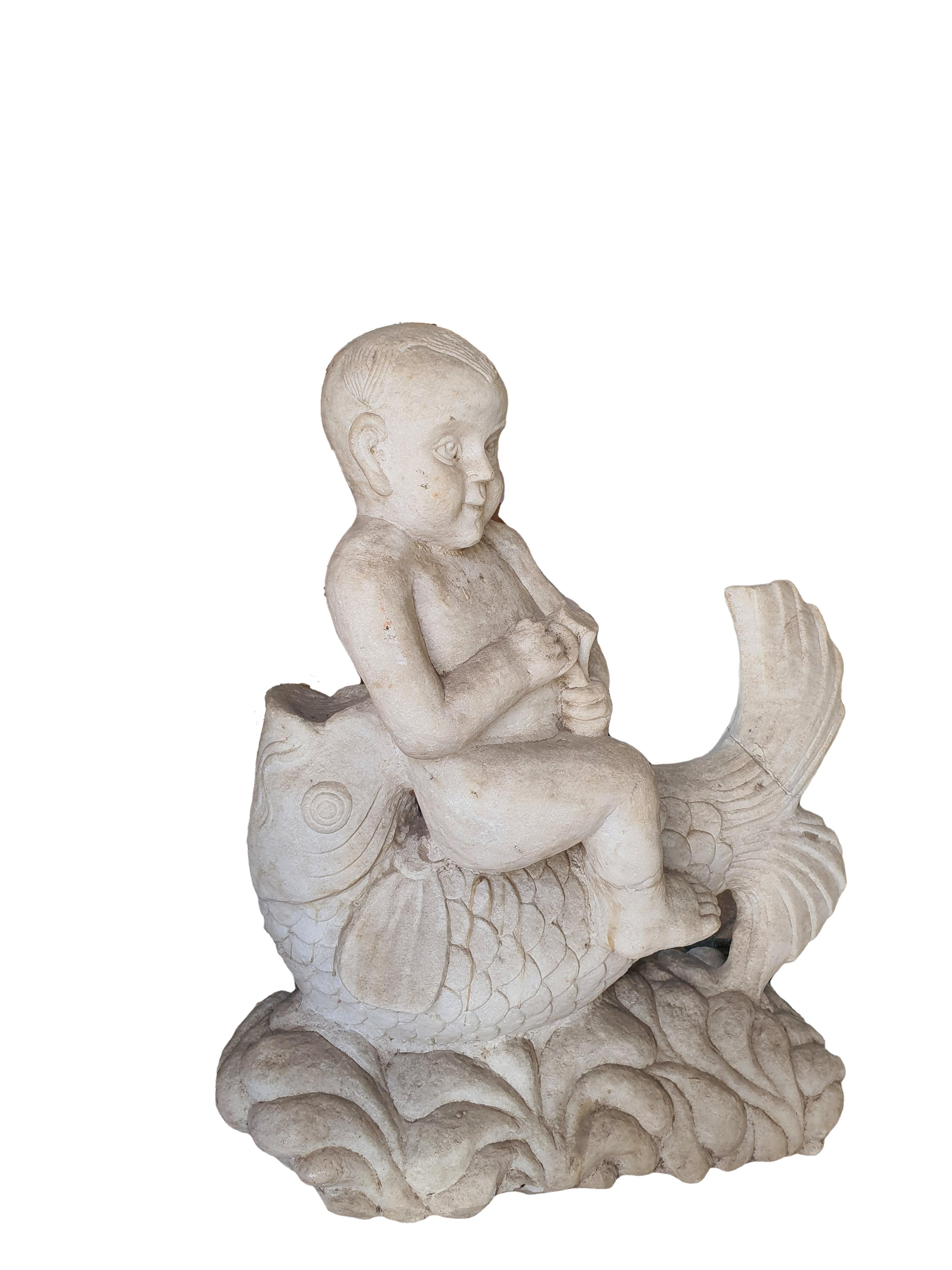 Elegant white statuary marble sculpture, carved from a single block of marble, depicting a cherub sitting on a sea fish. Finely carved in every detail.