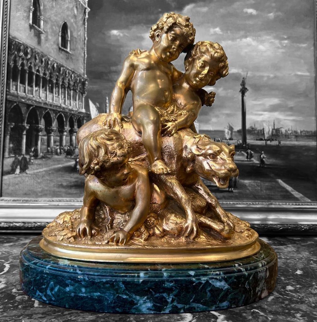 Nous vous présentons cette belle sculpture en bronze du XIXe siècle à la finition dorée, représentant un groupe de trois enfants jouant avec fougue avec une lionne. Notre statue est élégamment présentée sur un socle en marbre avec une anse en vert