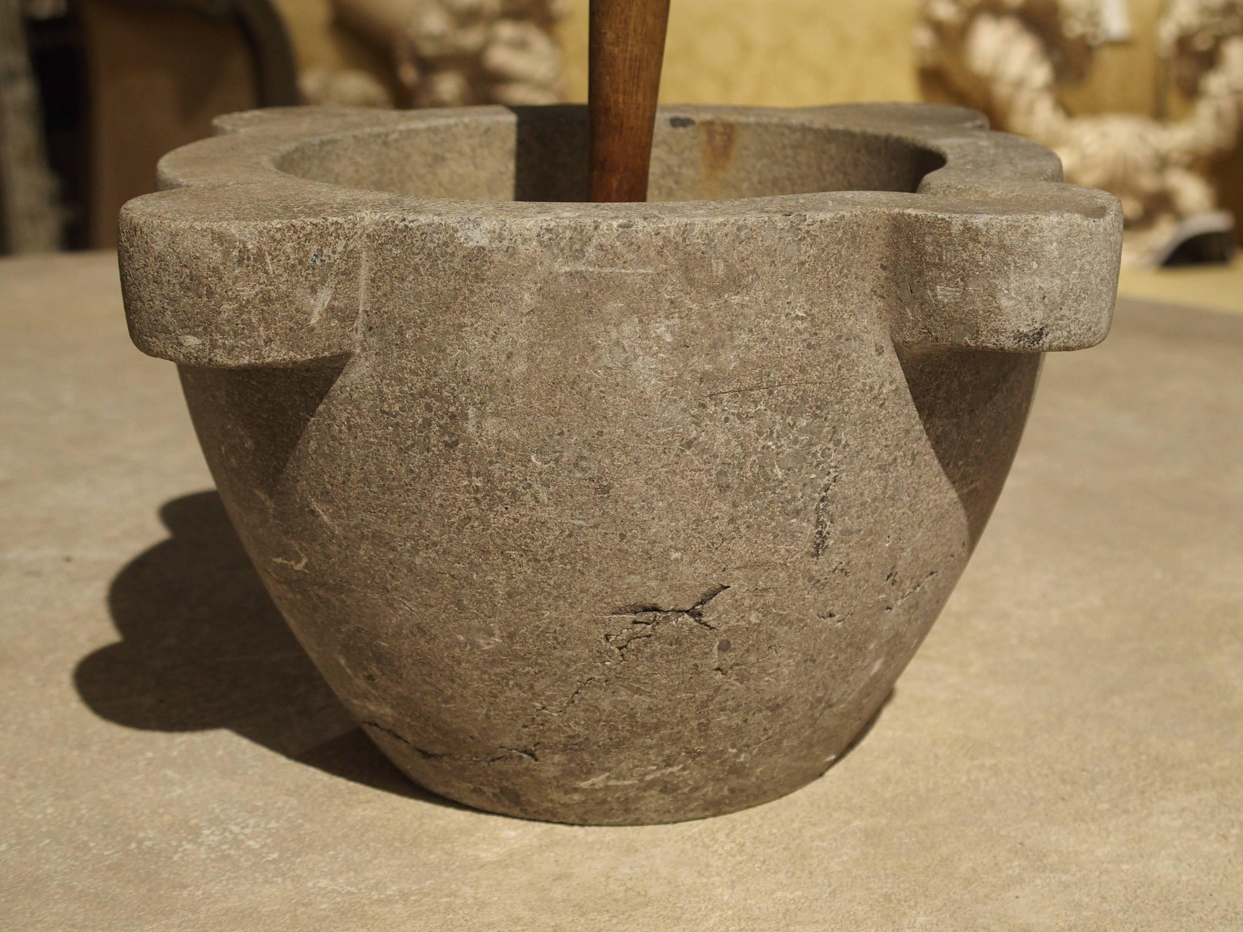 This stone mortar and wooden pestle is from France and dates to the 19th century. It is has four outturned motifs, one of which has an indented carved slot for easy pouring. The wooden pestle has a flat bottom.

 In France, these were used in the