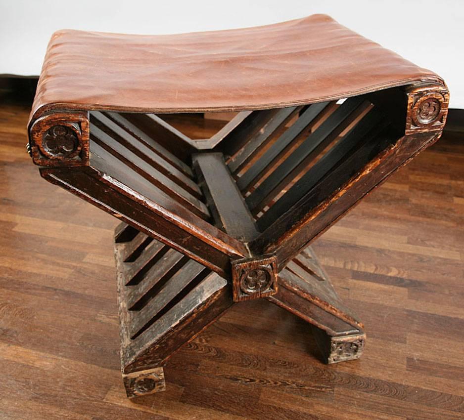 Tabouret de style Renaissance avec une assise en cuir tendue sur un cadre en forme de X. Les clous utilisés pour fixer le siège à la base sont en forme de fleur et les côtés du cadre sont sculptés. Les pieds et l'articulation centrale du tabouret