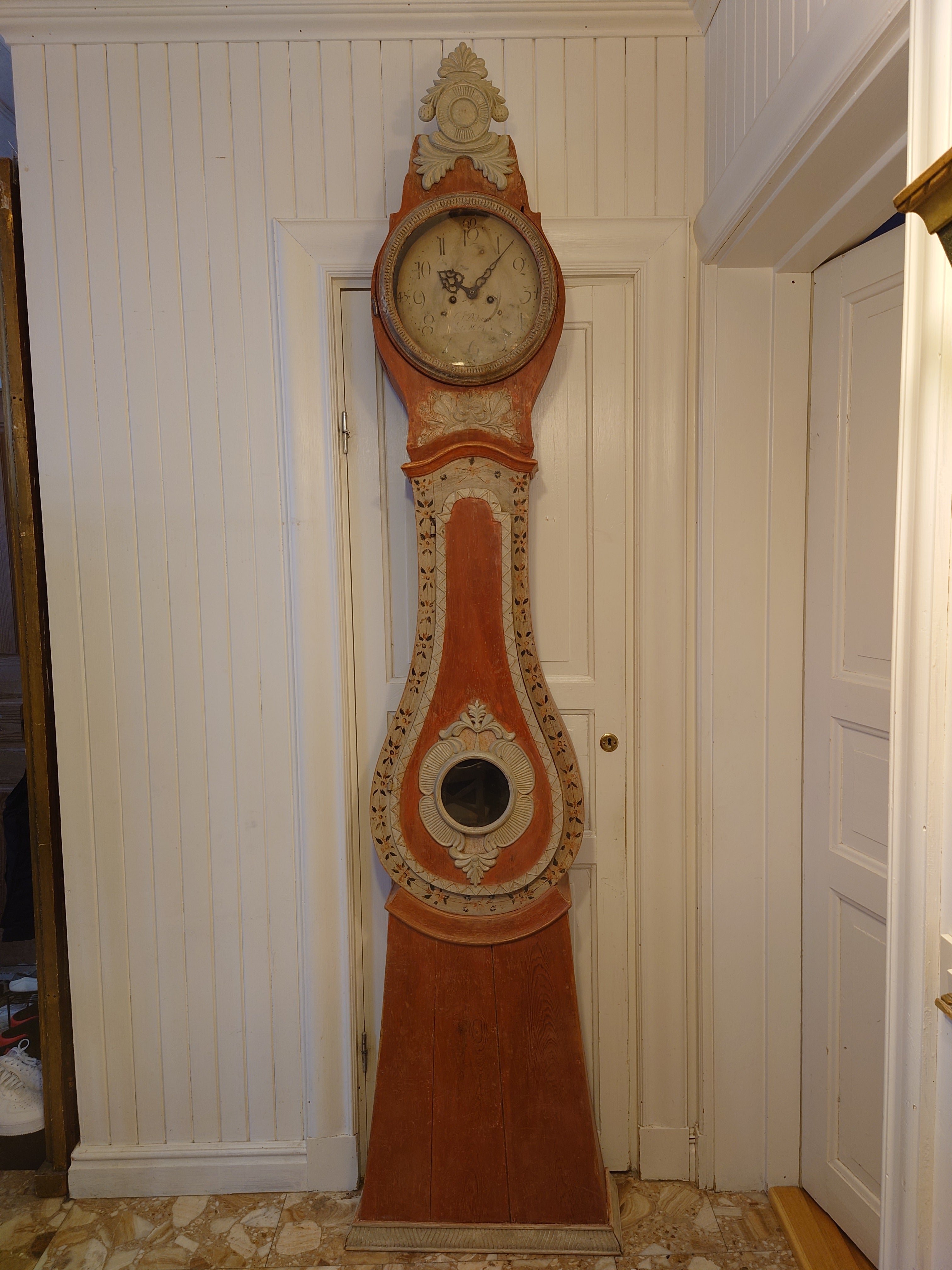 19th century Folk Art tall case clock from Luleå Norrbotten, Northern Sweden. Made in wood. Nice details and beautiful carvings. 
Beautiful handpainted flowers on the front. 
The Middle of the case has a windowed door to access the inside. 
This