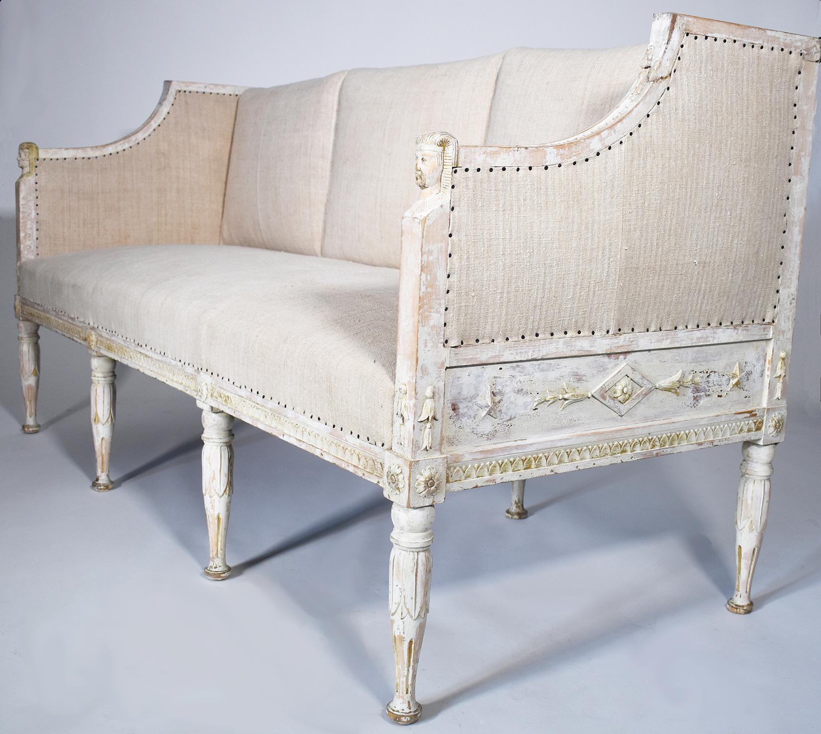 Stunning hand carved Swedish sofa with Egyptian influence and pale white grey patina over pine. Neoclassical carving detail on sides and legs. All pillows covered in a vintage European burlap.